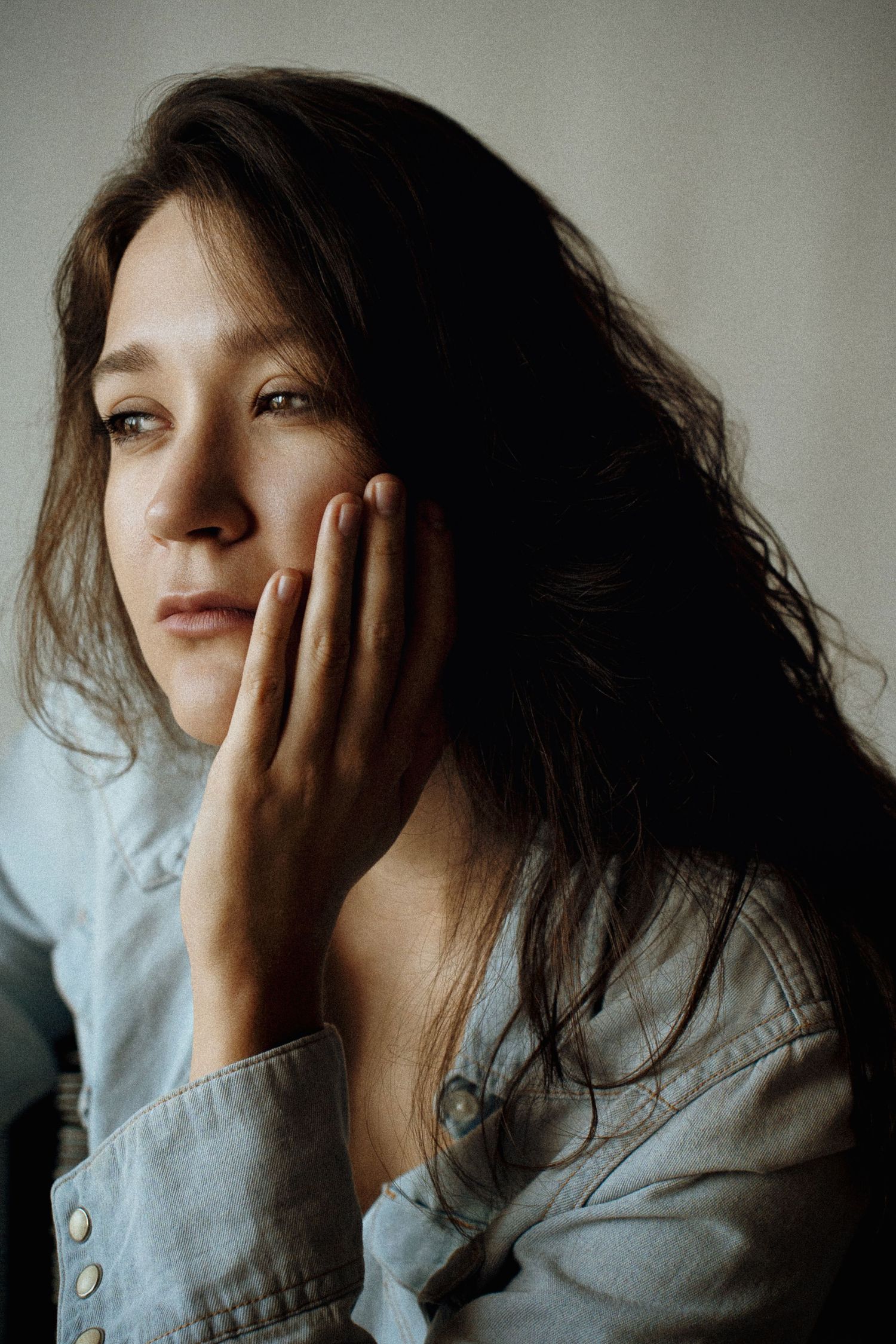 Portrait of a contemplative young woman with long brown hair resting her hand against her cheek.