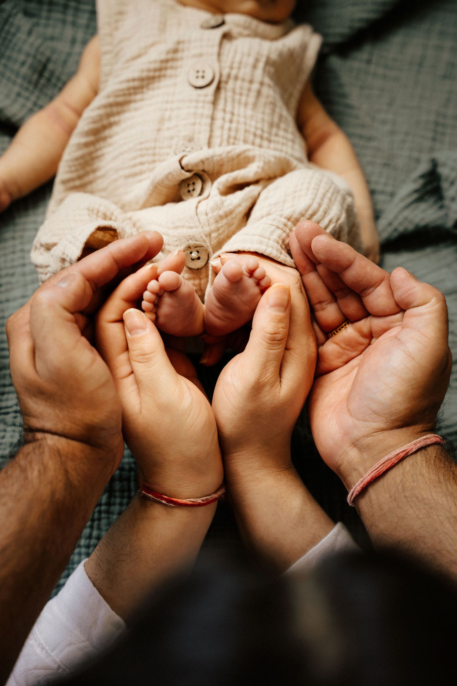 Two parents cradling their newborn baby's tiny feet in their hands, wearing matching red string bracelets.