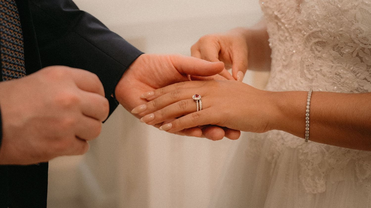 Bride and groom exchanging wedding rings during ceremony, close-up of hands with diamond engagement ring and bracelet.