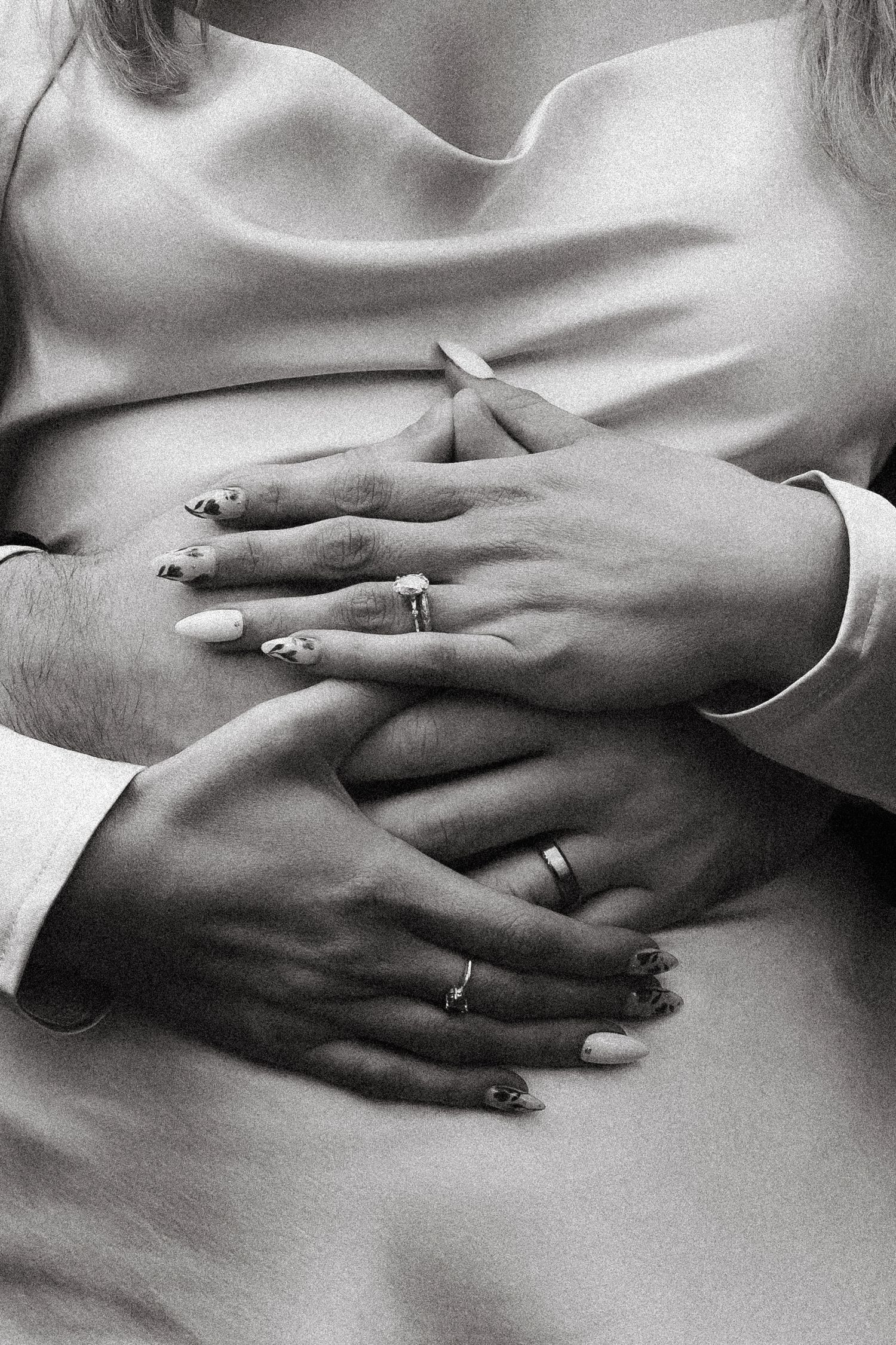 Black and white photo of a pregnant woman with her partner's hands resting on her baby bump, both wearing wedding rings.
