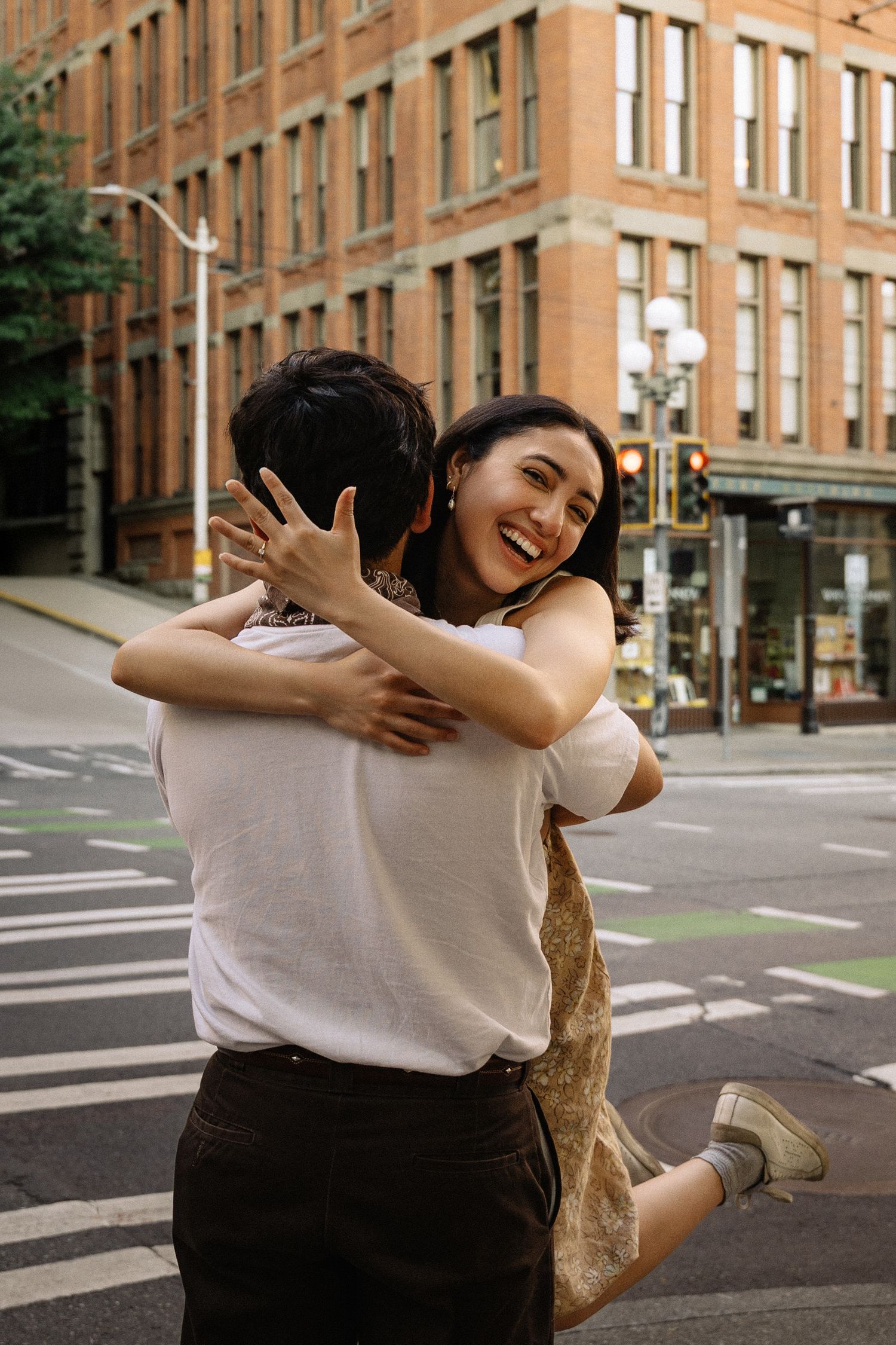 A laughing woman jumps into a mans arms while embracing on a city street corner.
