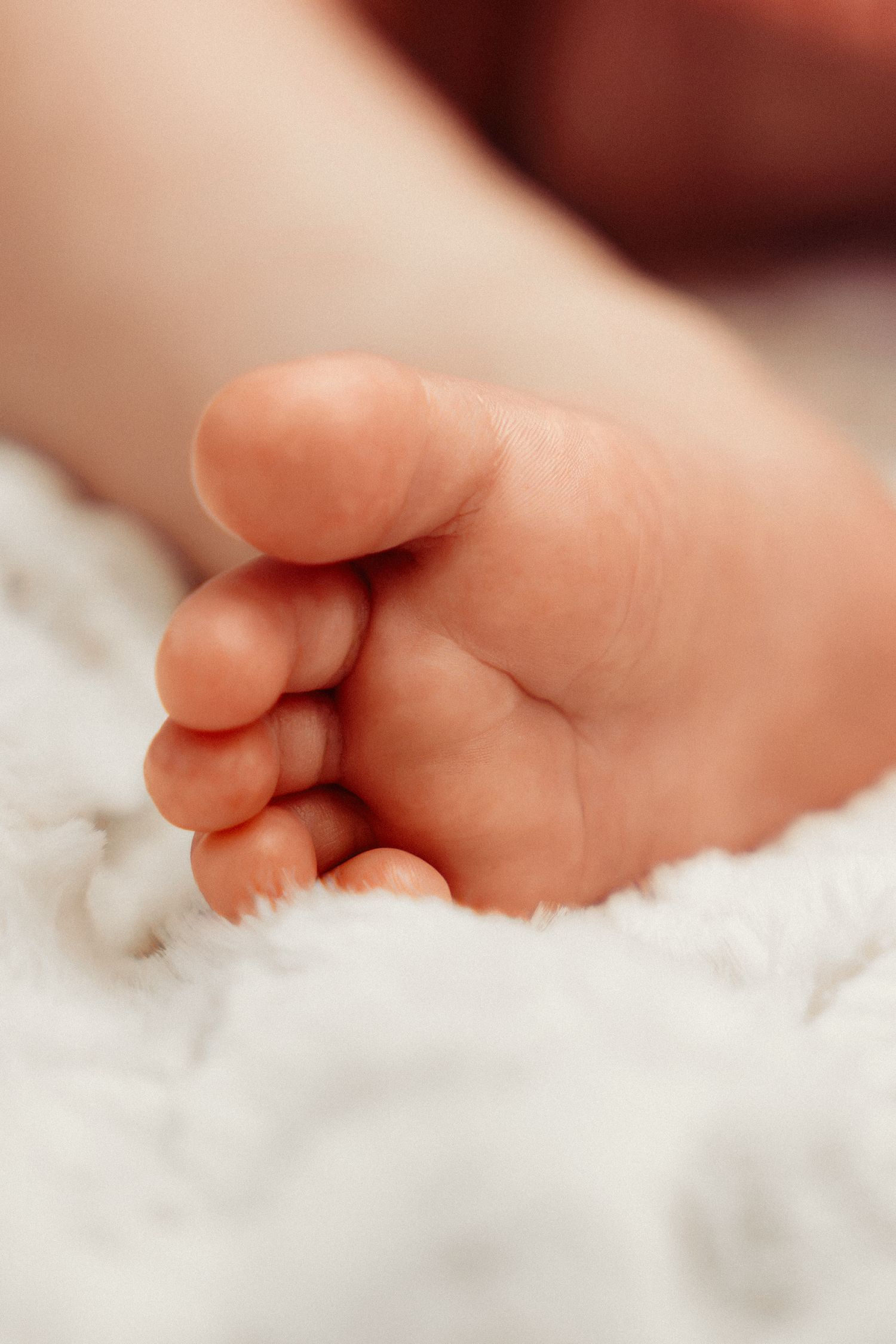 Close-up of a newborn baby's tiny foot resting on a soft white fluffy blanket.