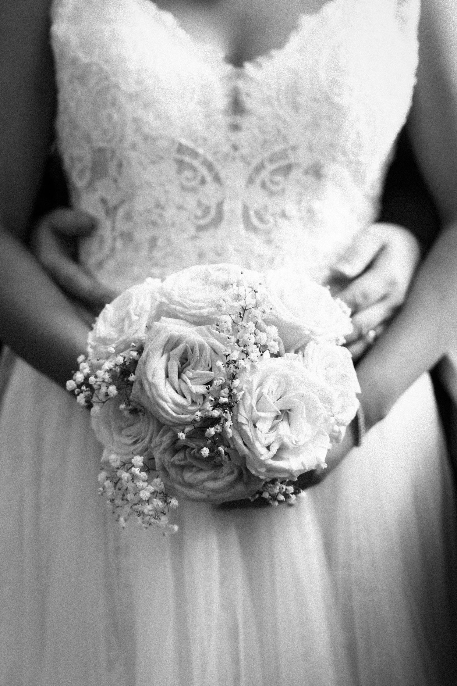 Black and white photo of a bride in lace gown holding a bouquet of roses and baby's breath.