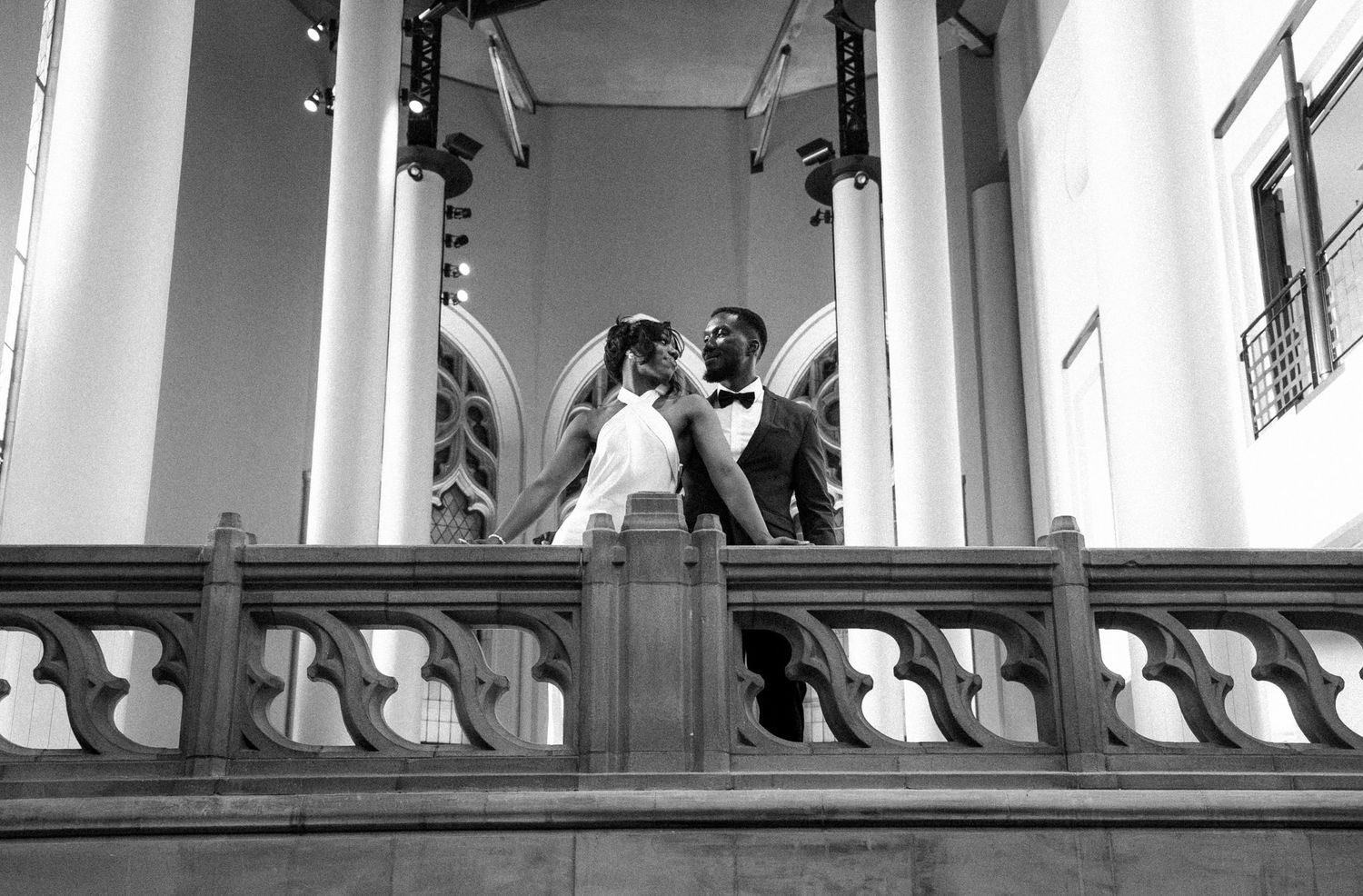 Black and white wedding photo of bride and groom sharing a romantic moment on an elegant balcony with tall columns Suzzallo Library.