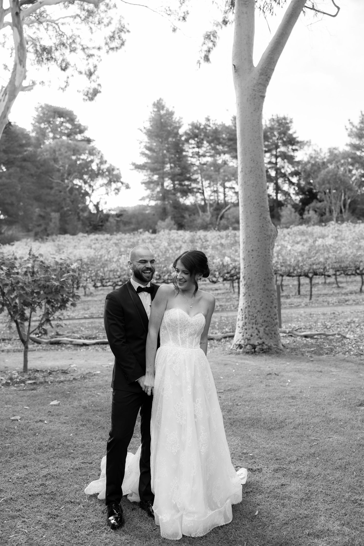 Black and white photo of bride and groom sharing a romantic moment among vineyard trees on wedding day.