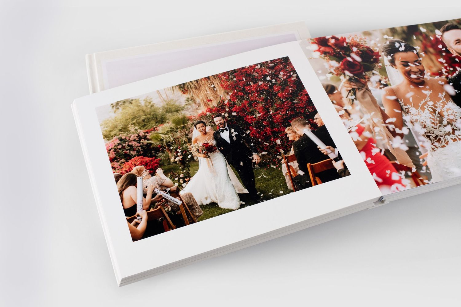 Open wedding photo album showing couple at outdoor ceremony surrounded by red flowers and confetti.
