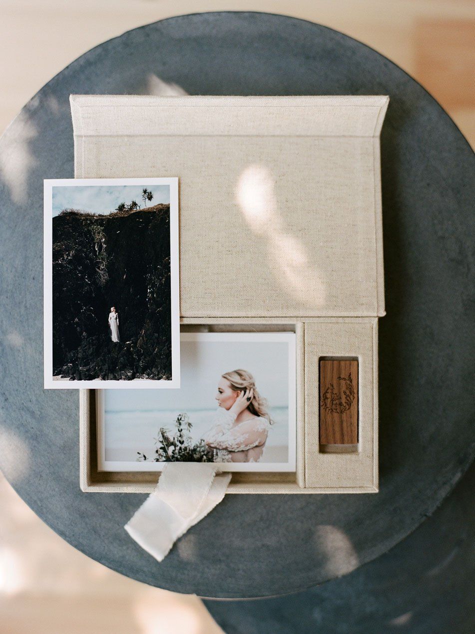 Linen photo box open on table with printed wedding photos, USB drive, and ribbon on marble surface.