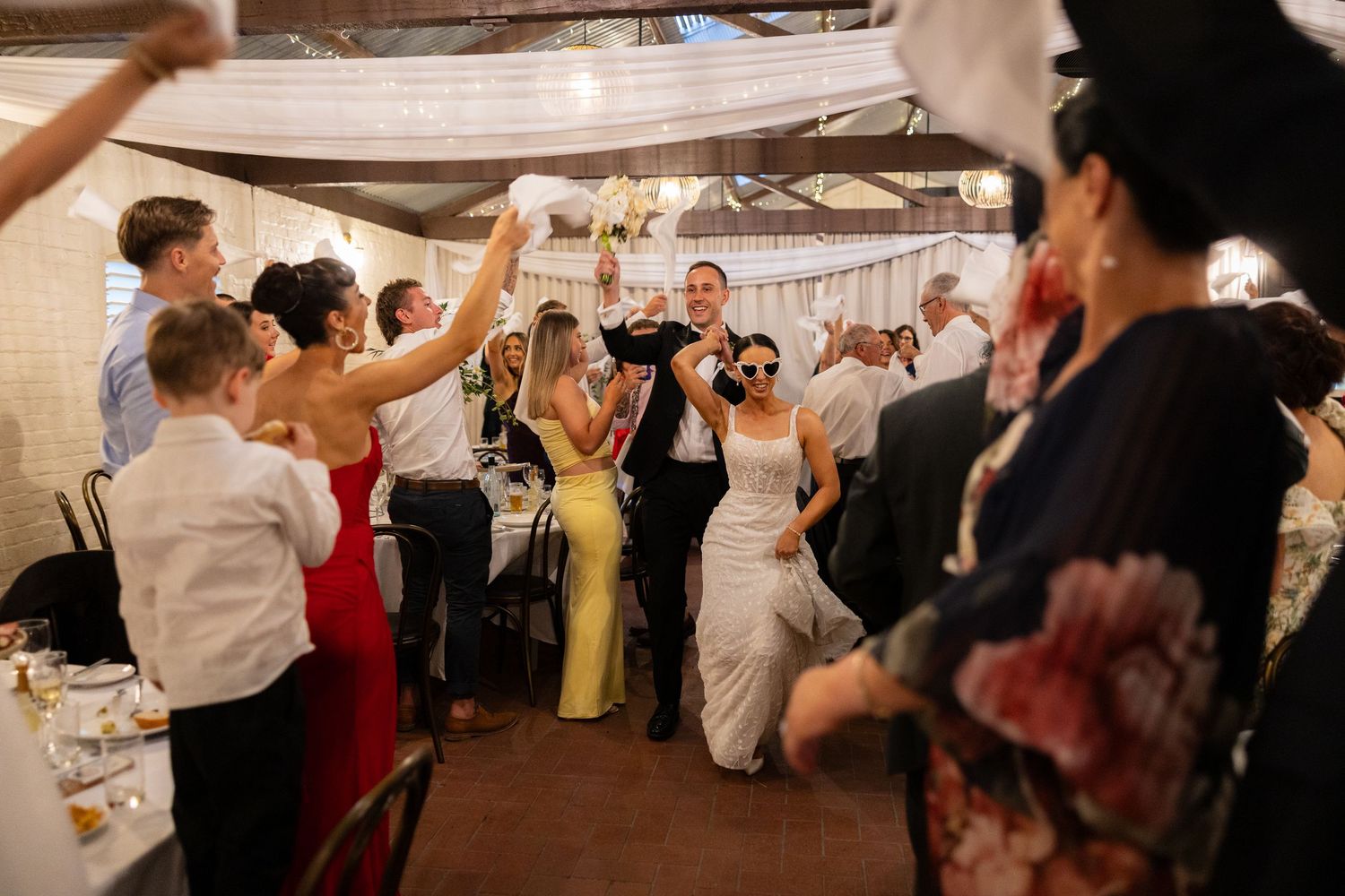 Bride and groom make grand reception entrance as guests celebrate in decorated wedding venue.
