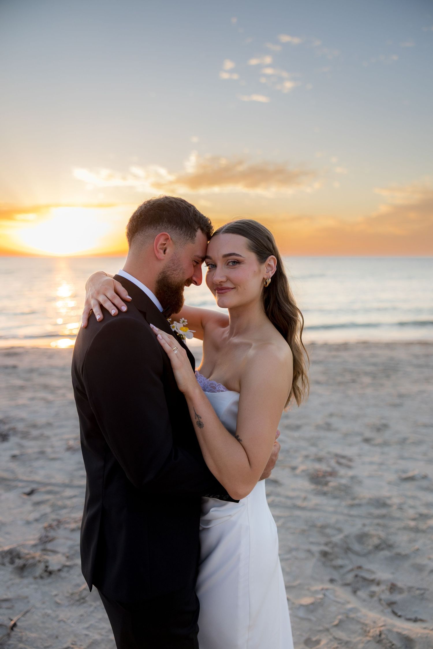 Newlywed couple embrace romantically on a sandy beach during a stunning golden sunset.