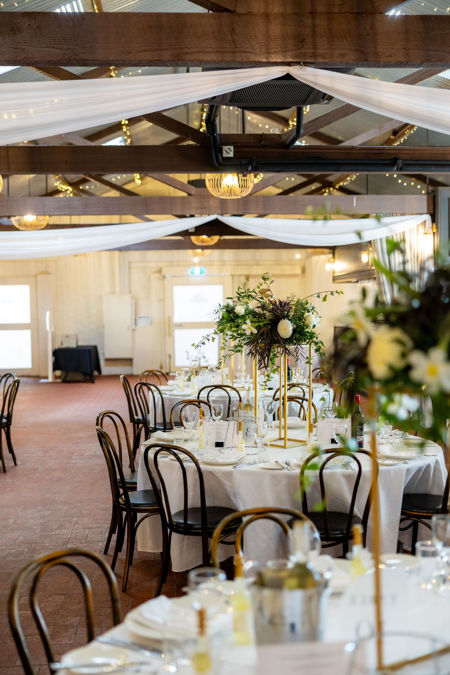 Elegant wedding reception venue with white draped ceilings, fairy lights, and gold floral centerpieces.