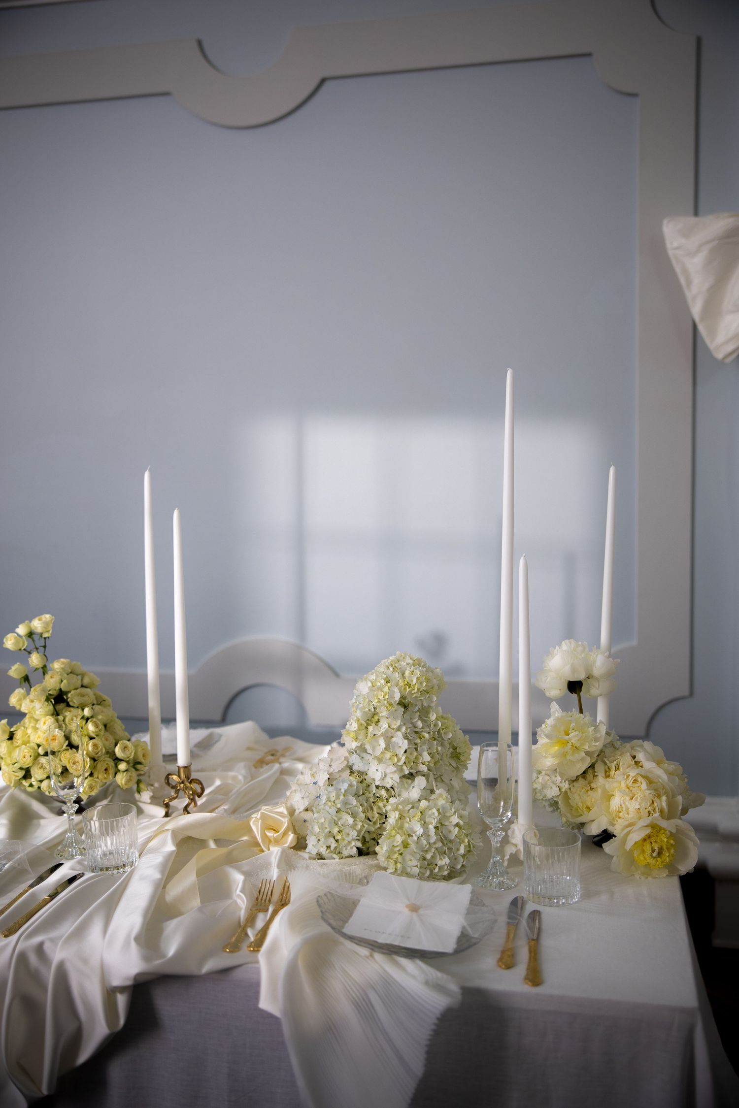 Elegant wedding sweetheart table with white hydrangea centerpieces, tall taper candles, and gold cutlery.