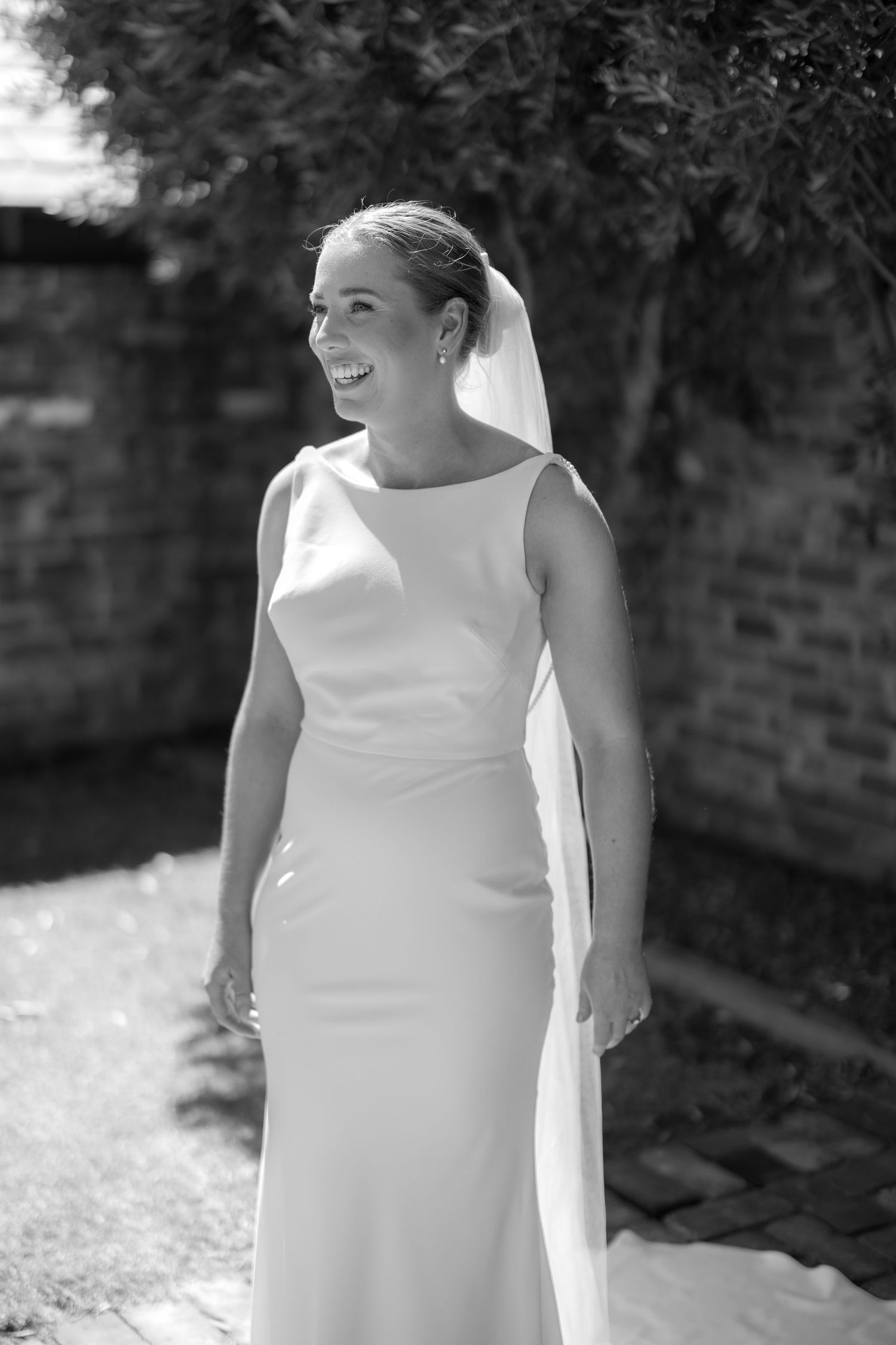 Black and white portrait of laughing bride in sleeveless wedding dress with veil outdoors.
