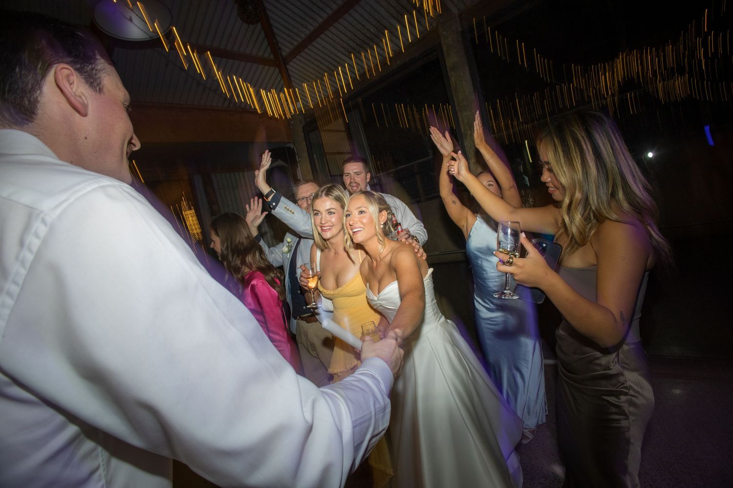 Bride and guests dancing joyfully at a wedding reception under a thatched roof venue.