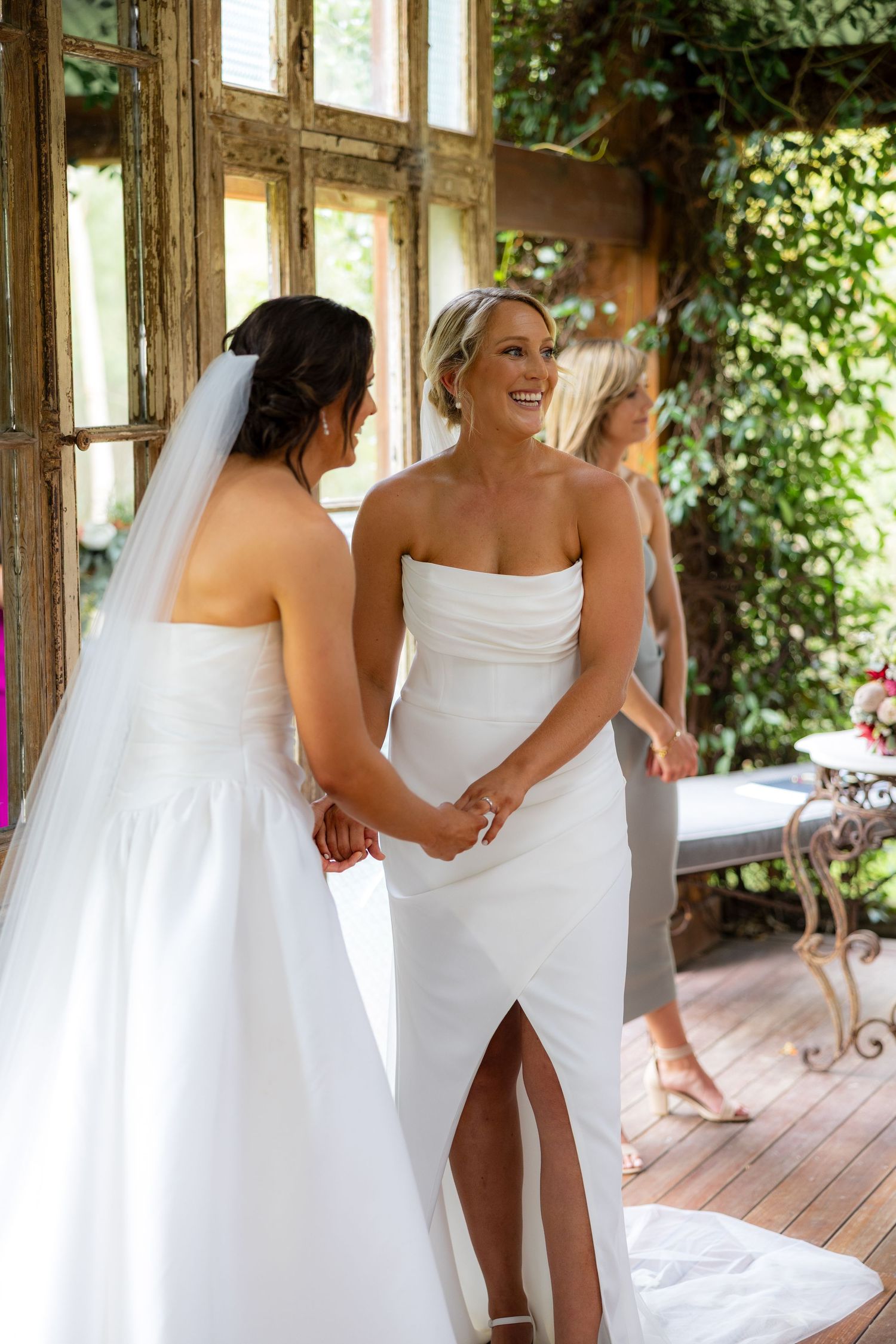 Two brides share an emotional first look moment holding hands and smiling at each other on their wedding day.