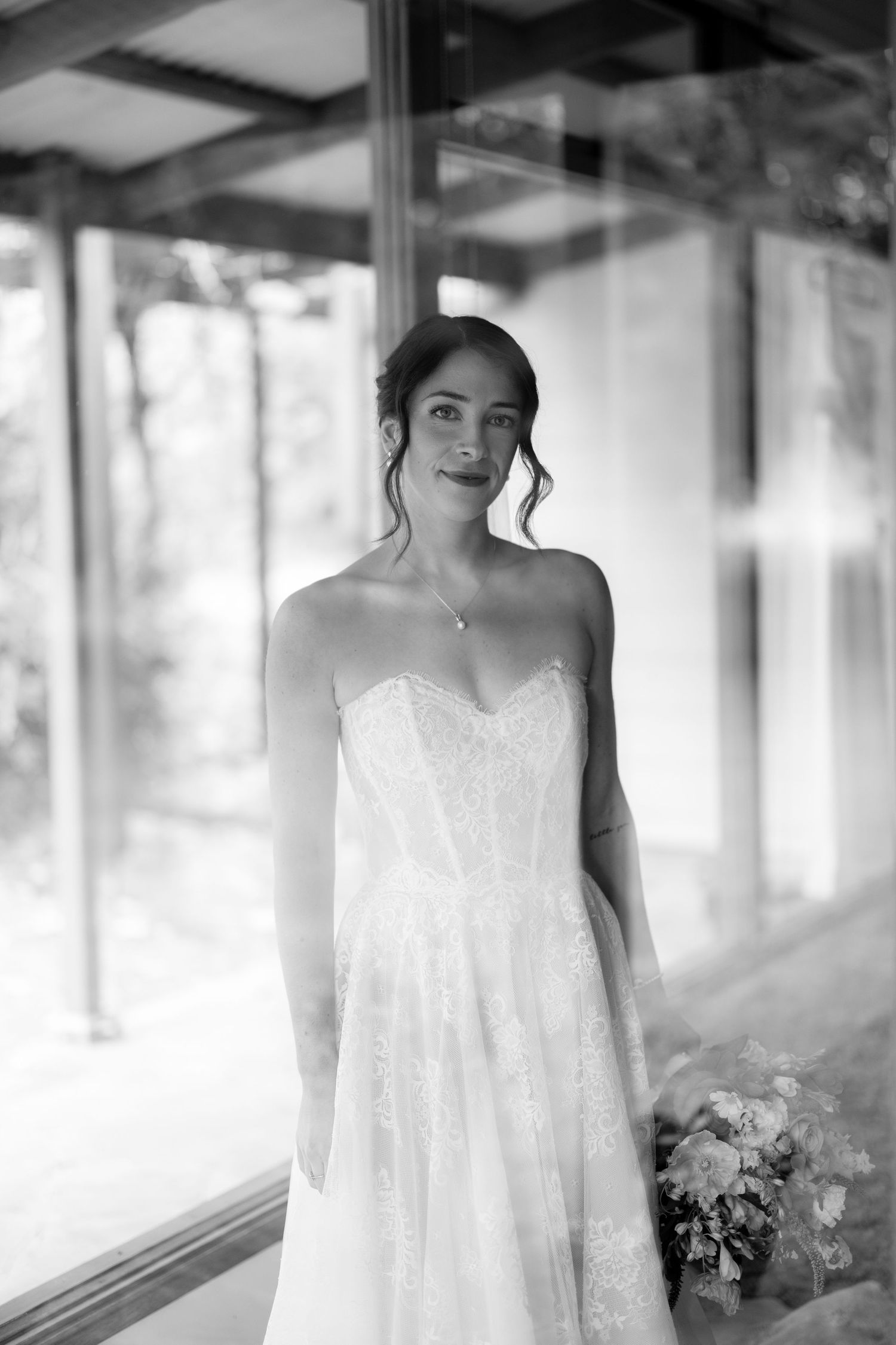 Elegant bride in strapless lace wedding gown poses with bouquet in black and white portrait.
