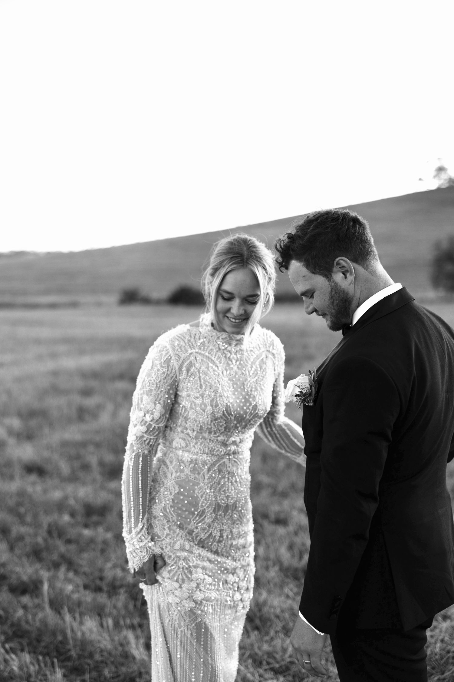 Bride and groom share a joyful moment in a field at sunset, bride wearing beaded lace gown.