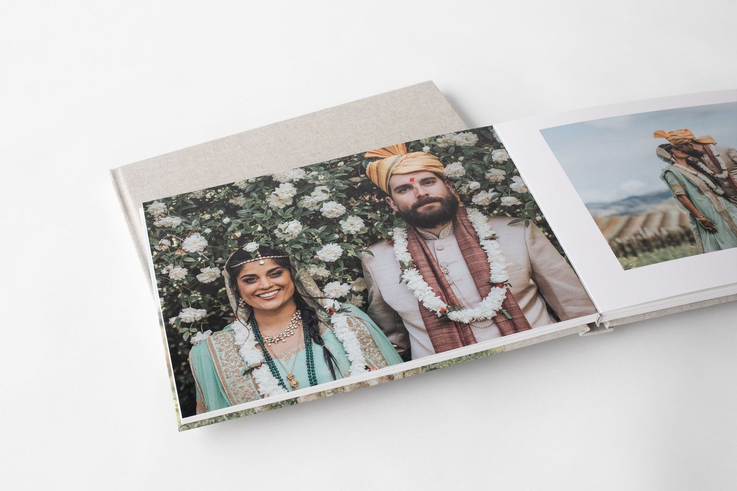 Open wedding album displaying portrait of Indian bride and groom in traditional attire outdoors.