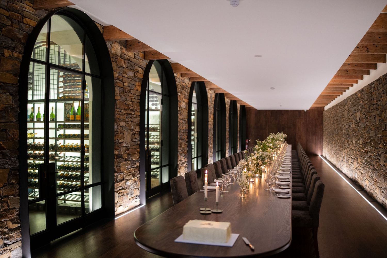 Long elegant dining table set for a wedding reception in a modern stone wine cellar.