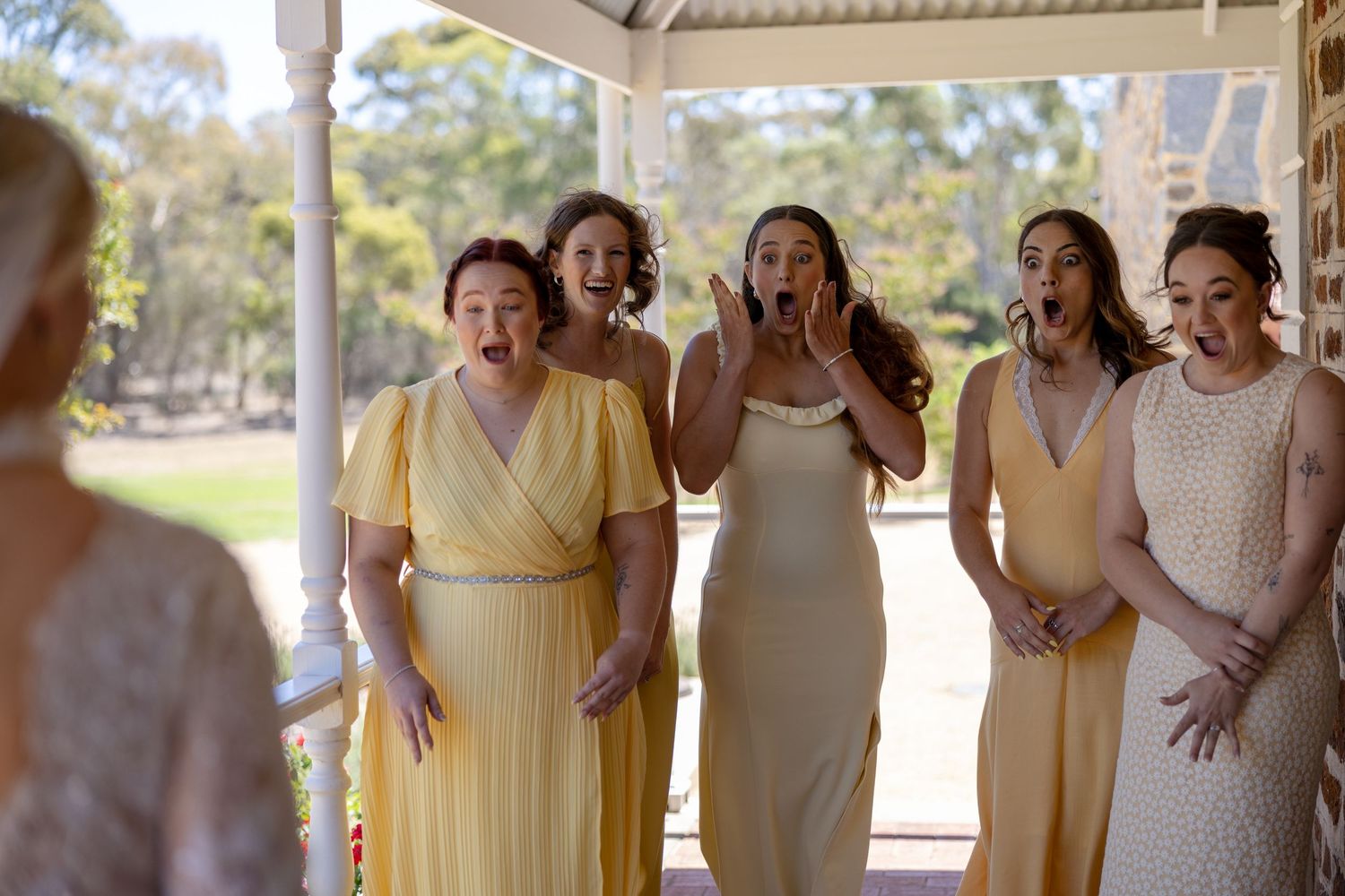 Five bridesmaids in yellow dresses react with joy and surprise during bride's first look reveal.