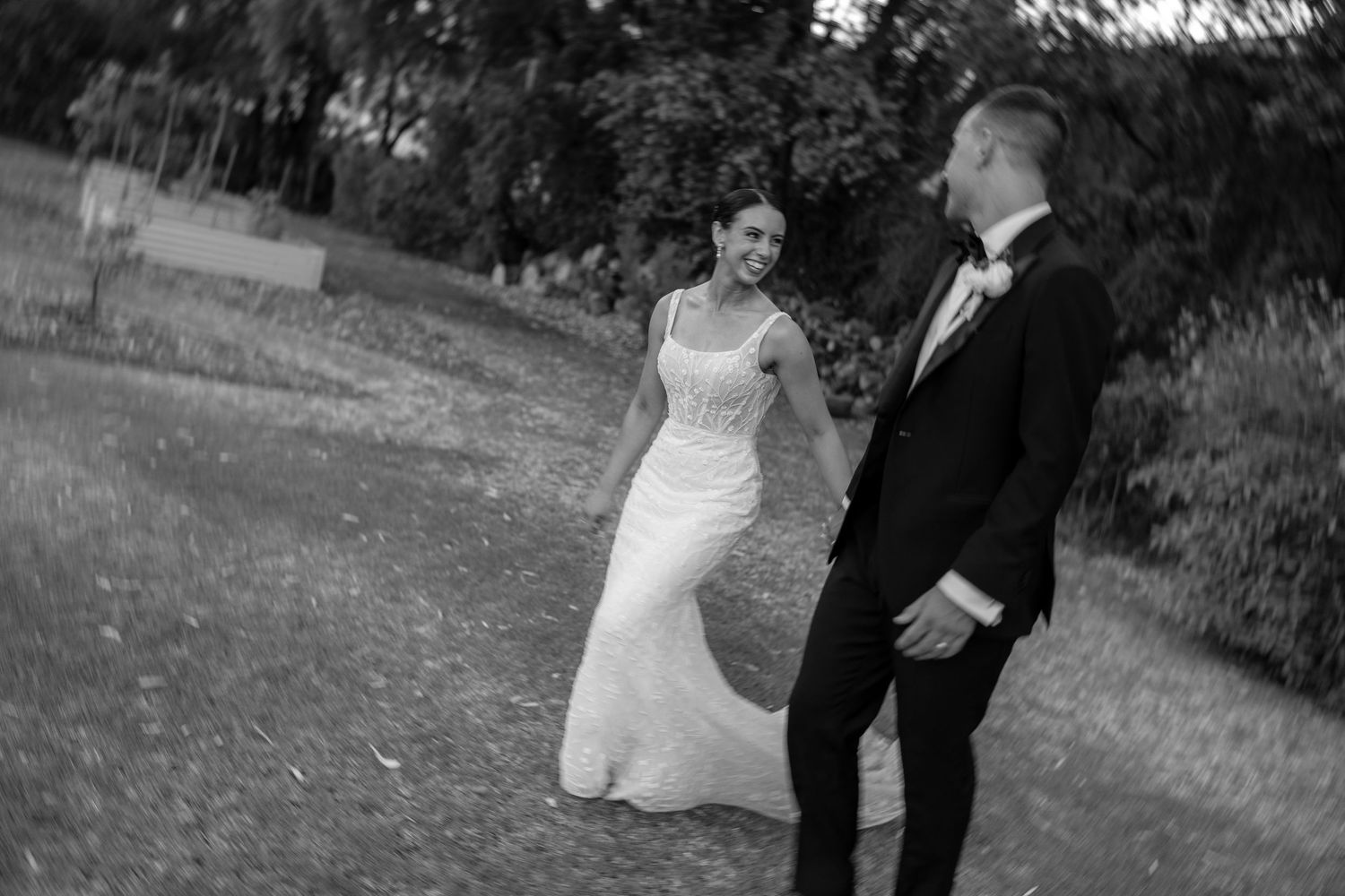 Bride and groom sharing a joyful moment walking through a garden in black and white wedding photo.