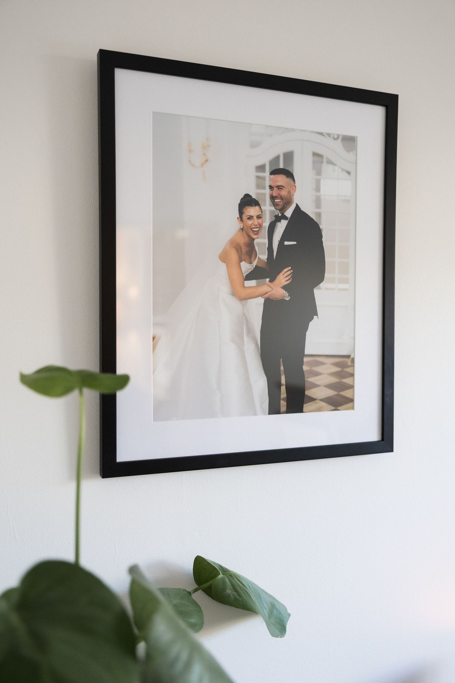 Close-up of framed bride and groom wedding portrait in black frame on white wall.