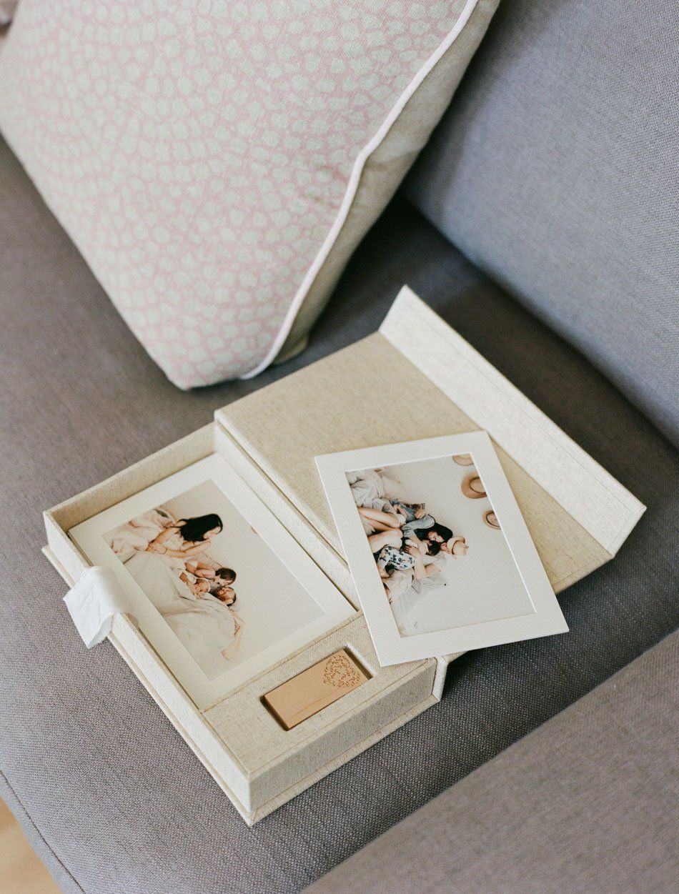 Open linen photo box on sofa with printed photos and wooden USB drive, casual lifestyle display.