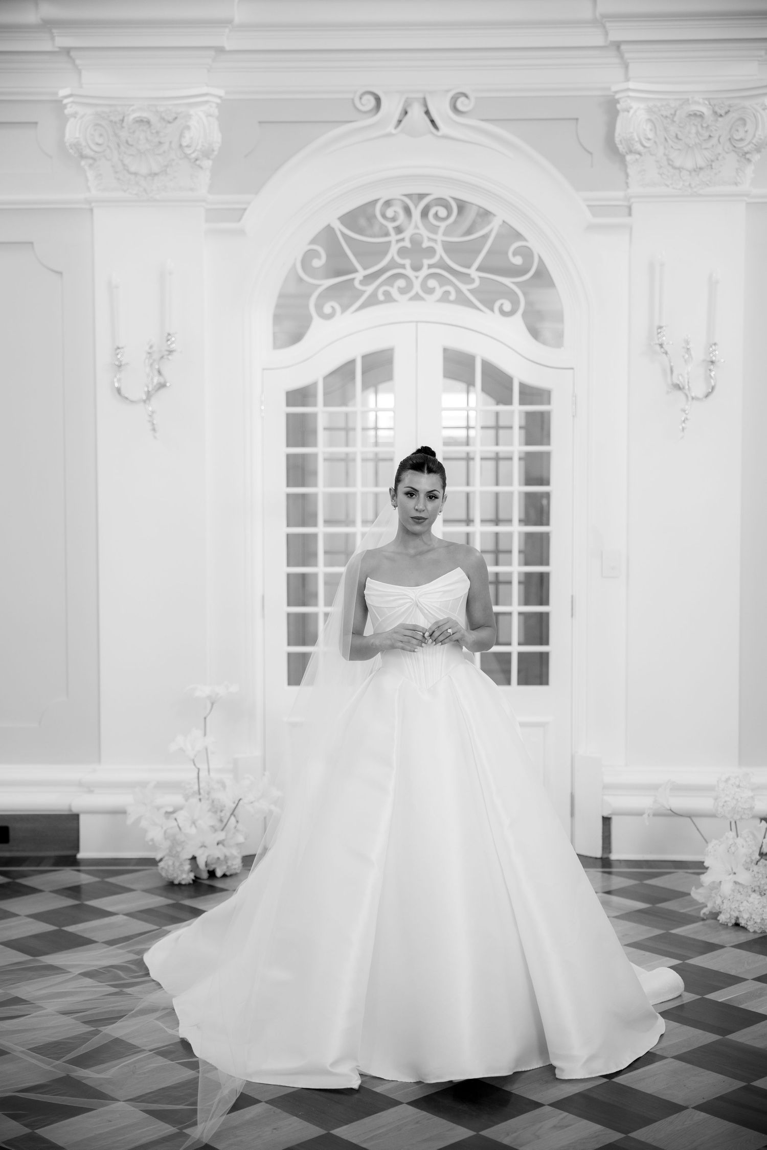 Bride in strapless ballgown wedding dress poses in elegant black and white photo before ornate French doors.