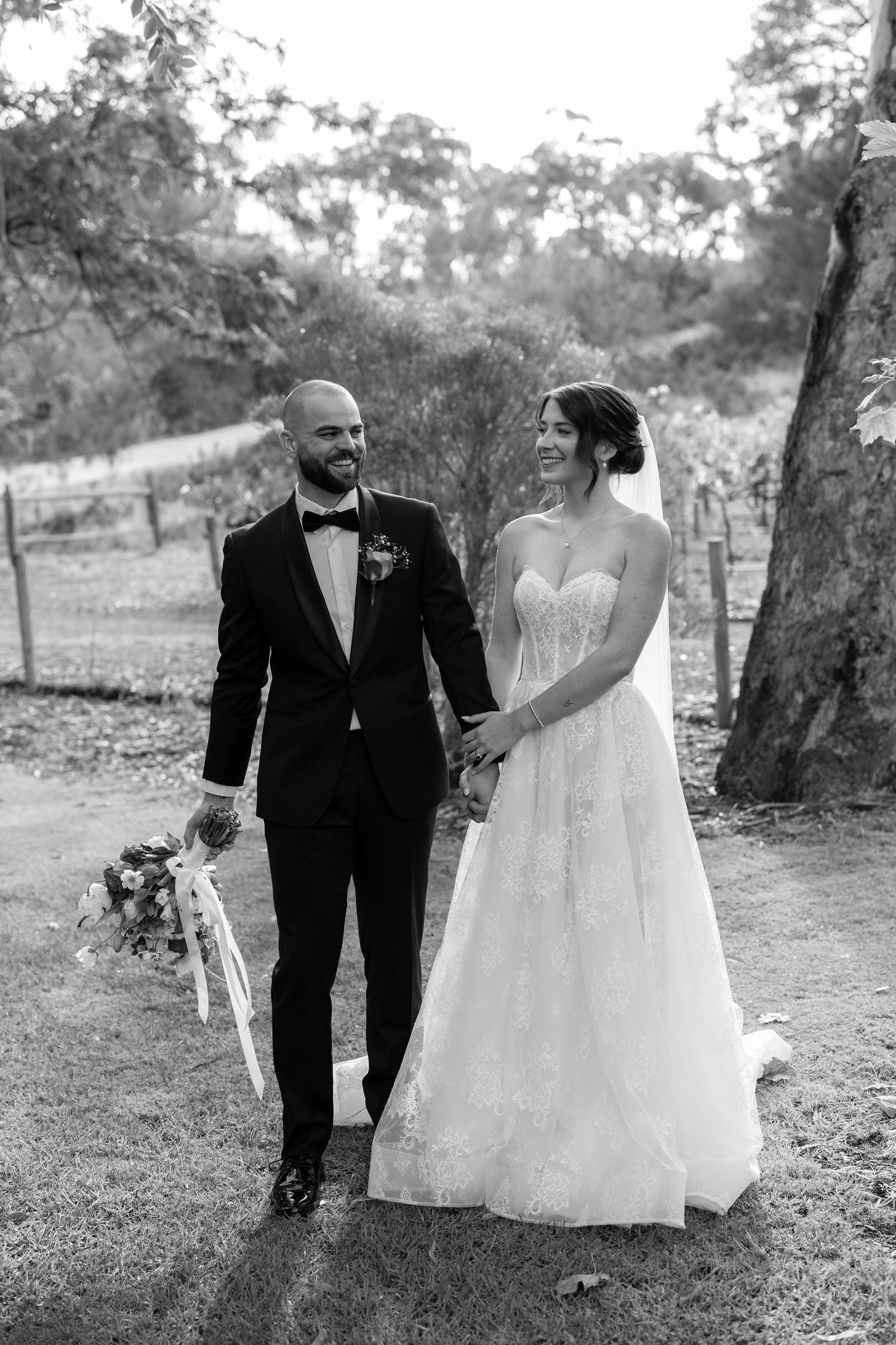 Bride and groom walking hand in hand through vineyard in elegant black and white portrait.
