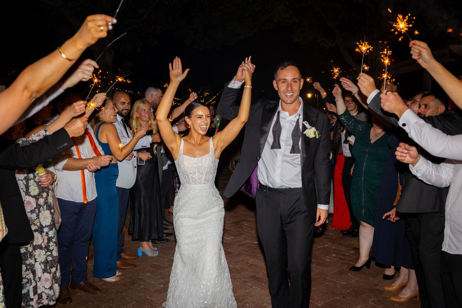 Bride and groom walking through a sparkling sparkler exit tunnel with cheering guests at their wedding reception.