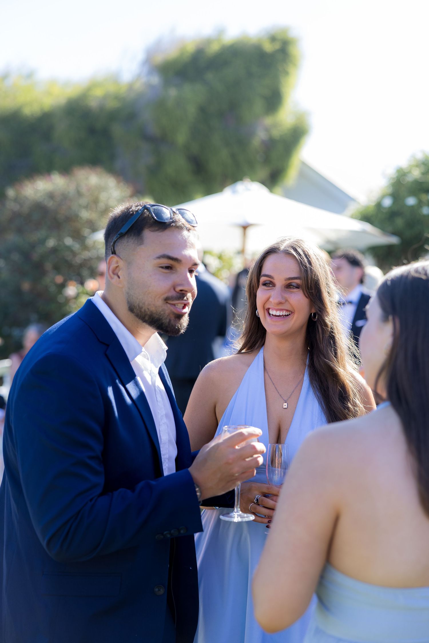 Smiling couple in blue attire holding champagne glasses at an outdoor wedding reception.