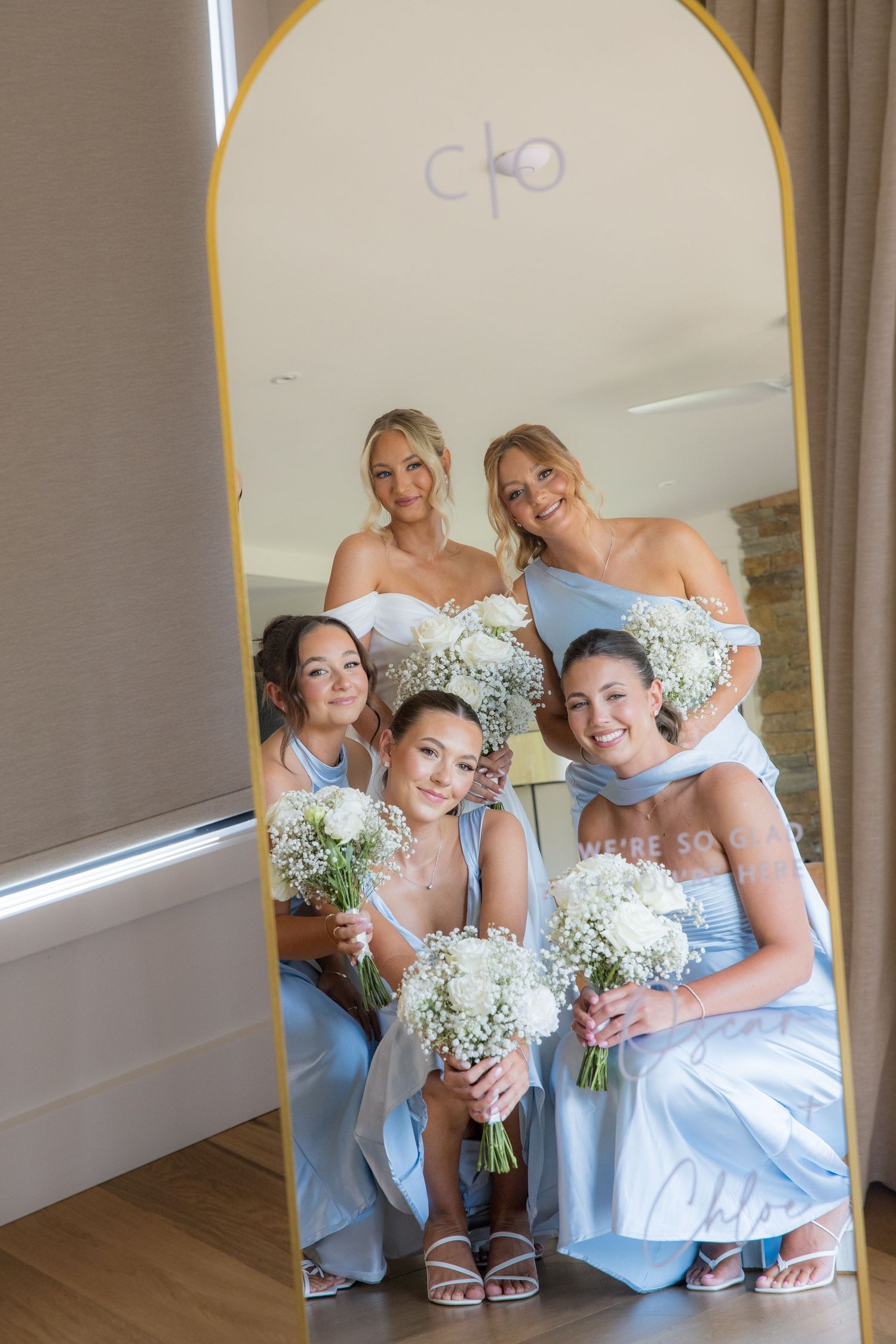 Bride and four bridesmaids in light blue dresses posing together in a mirror reflection.