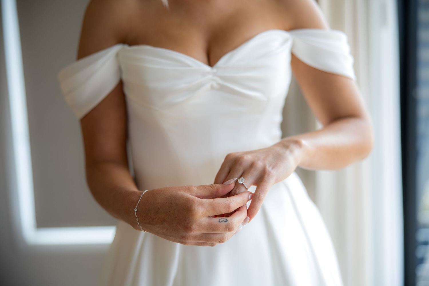 Close-up of bride in white off-shoulder wedding gown adjusting her diamond engagement ring.