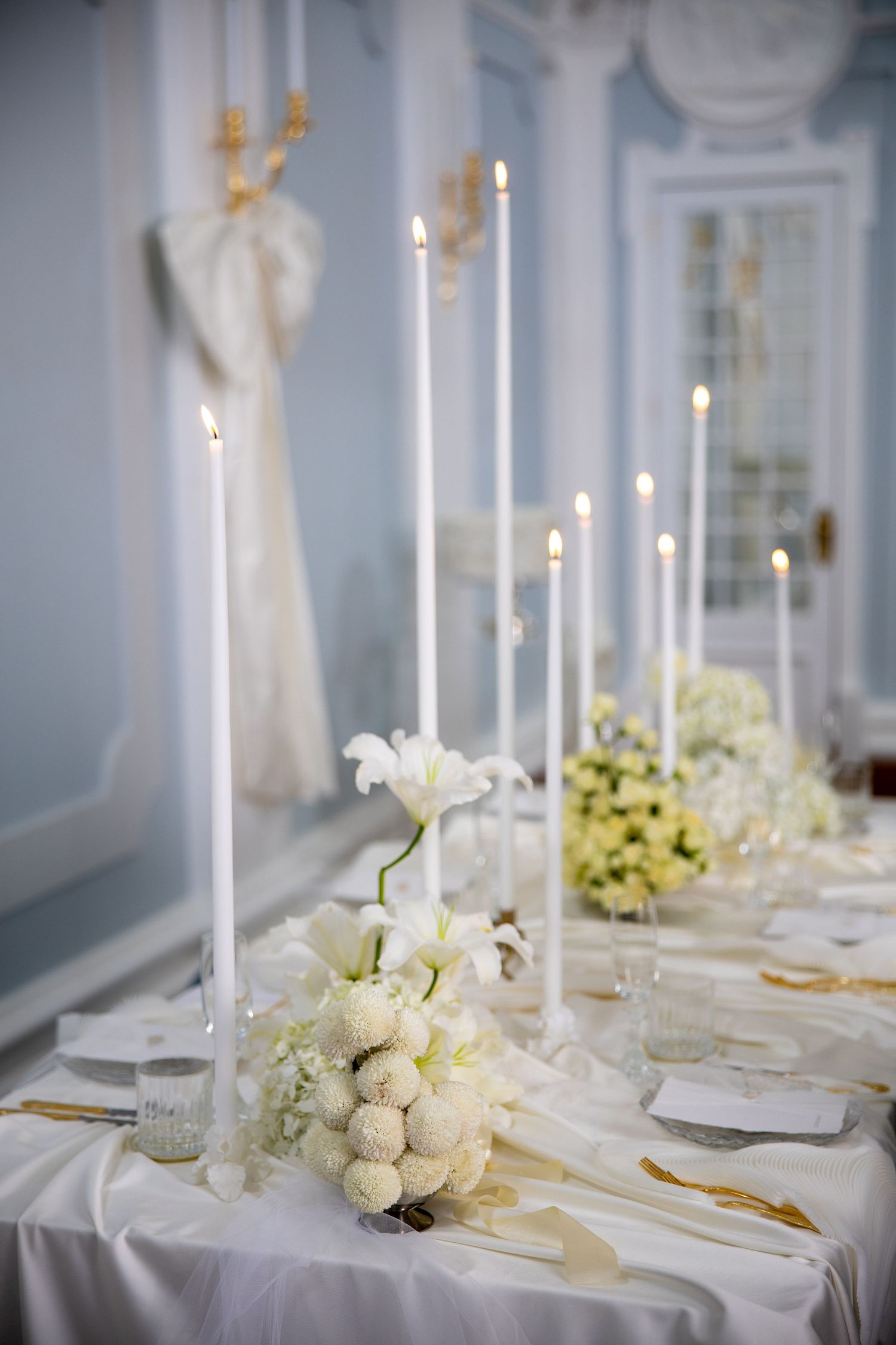 Elegant wedding reception table with tall white taper candles and white floral centerpieces on a draped white tablecloth.