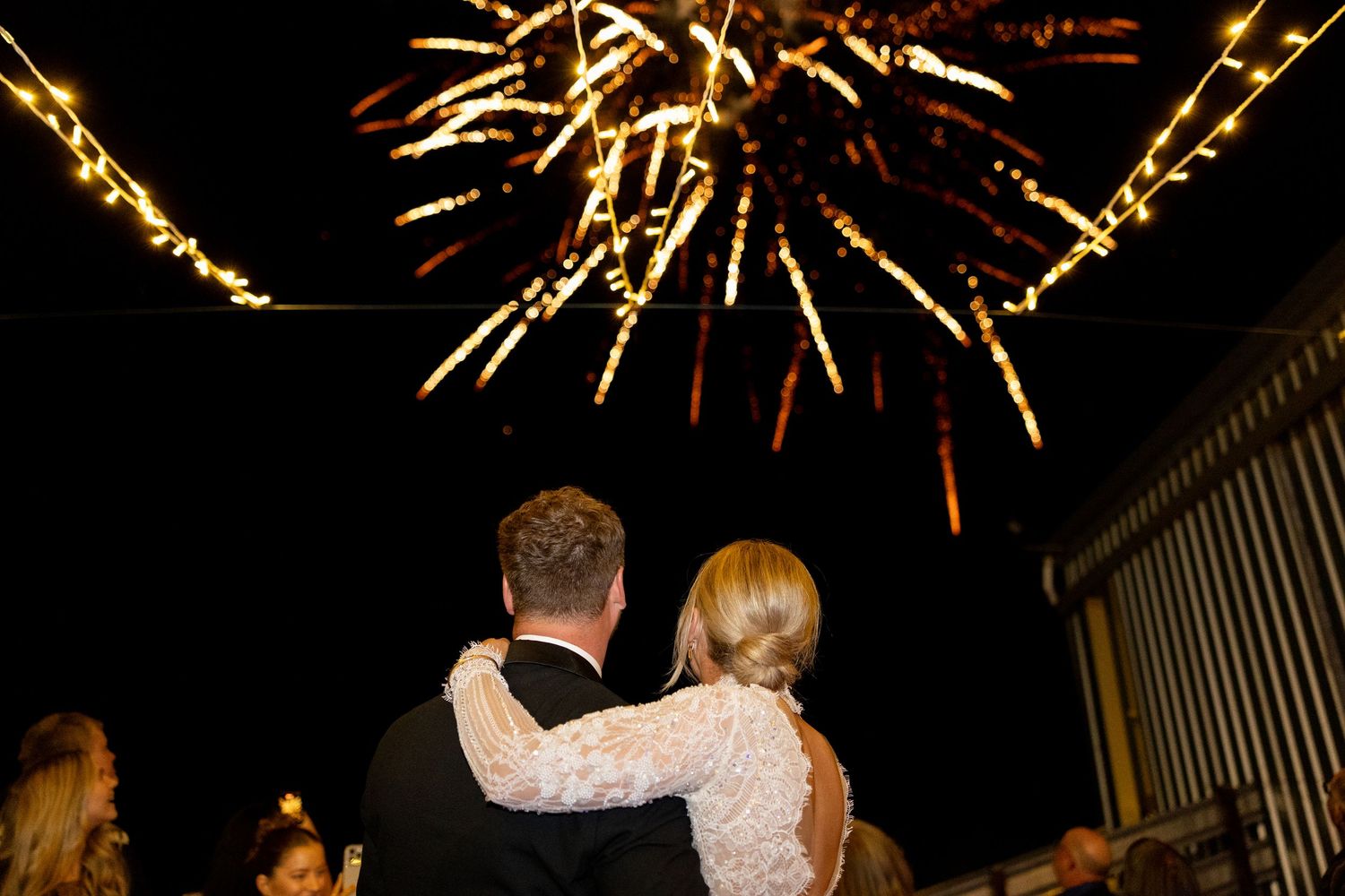 Bride and groom watch a stunning fireworks display light up the night sky at their wedding.