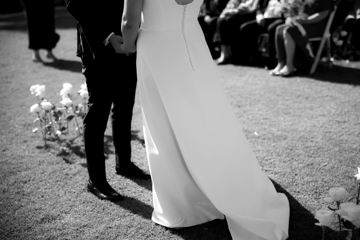 Black and white photo of bride and groom holding hands during outdoor wedding ceremony.