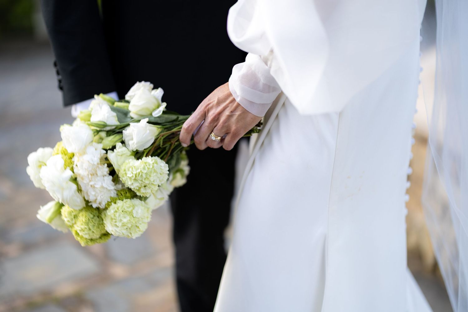 Close-up of bride and groom holding a white and green bouquet with diamond ring visible.
