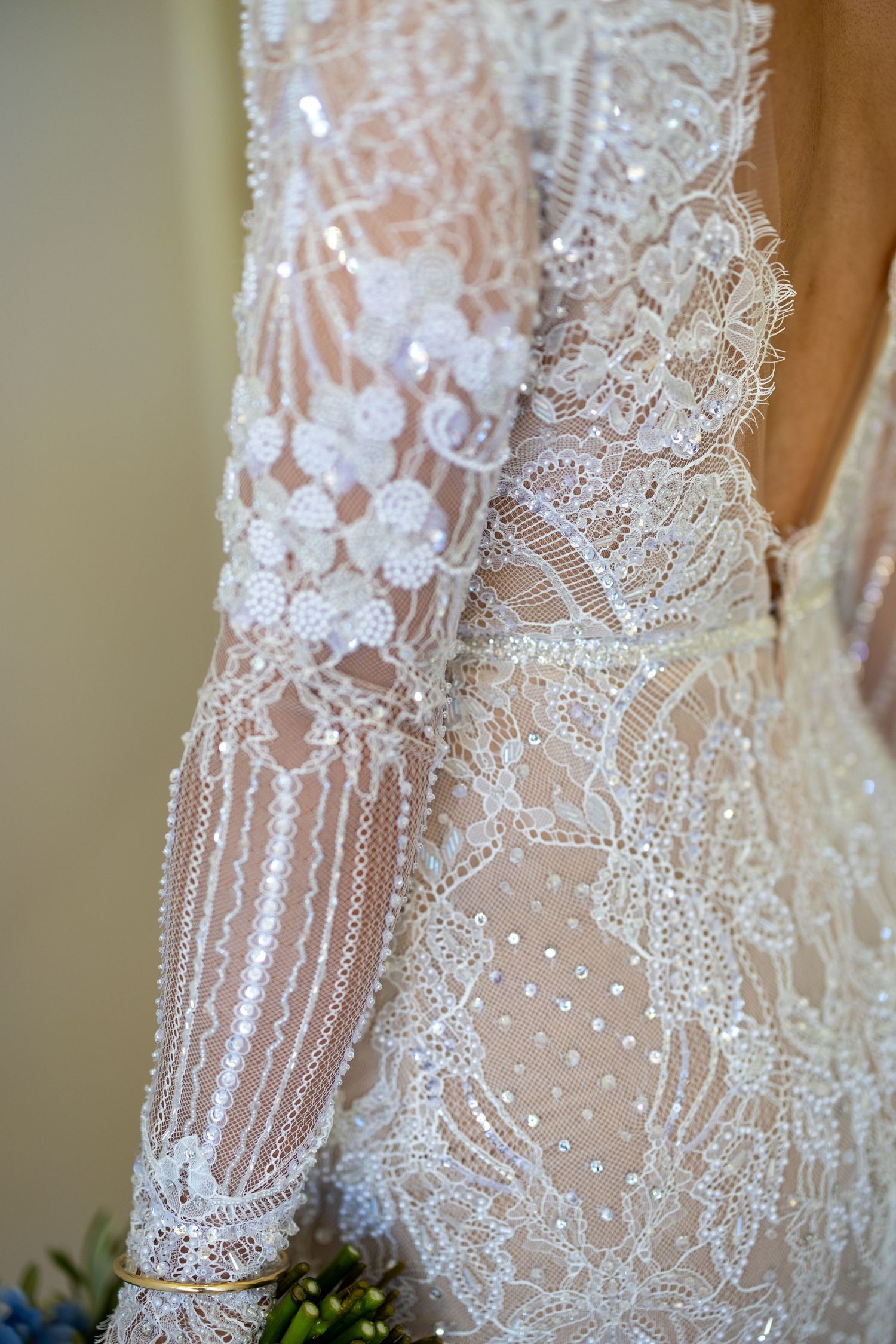 Close-up detail of a heavily beaded and embroidered sheer lace long-sleeve bridal gown.