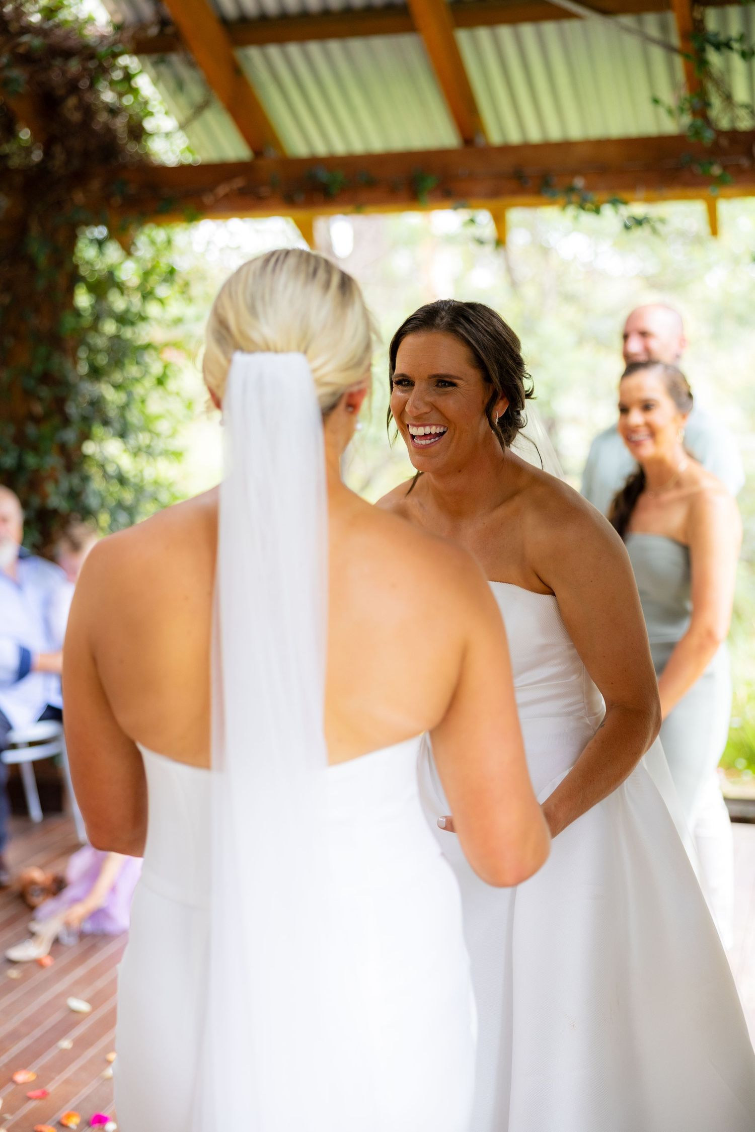 Two brides share a joyful moment at the altar during their wedding ceremony in a rustic outdoor pavilion.