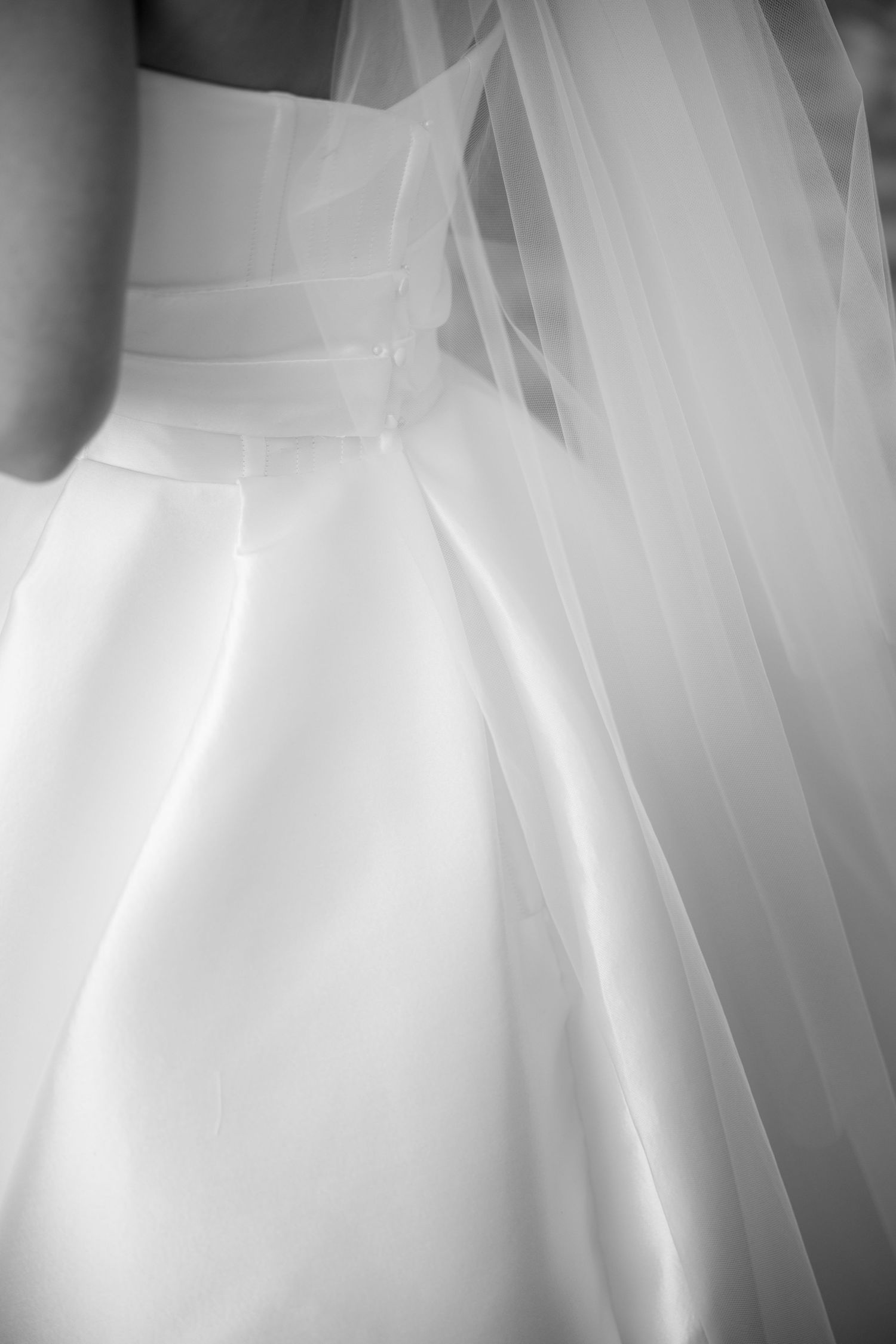 Black and white close-up detail of white satin wedding dress with flowing tulle veil.