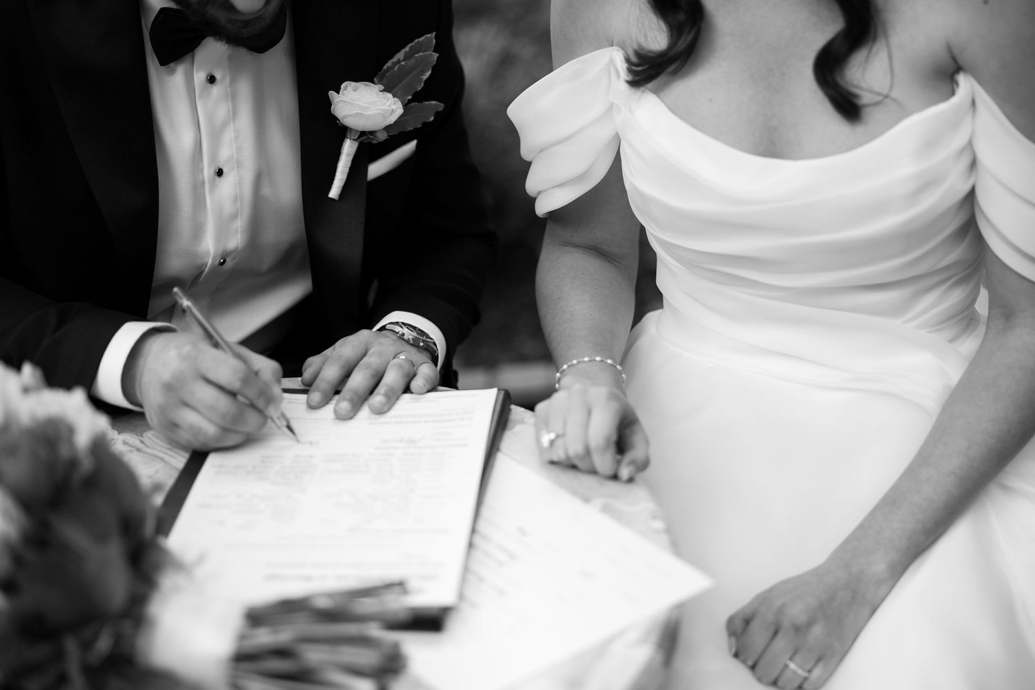 Black and white photo of bride and groom signing wedding certificate at elegant ceremony.