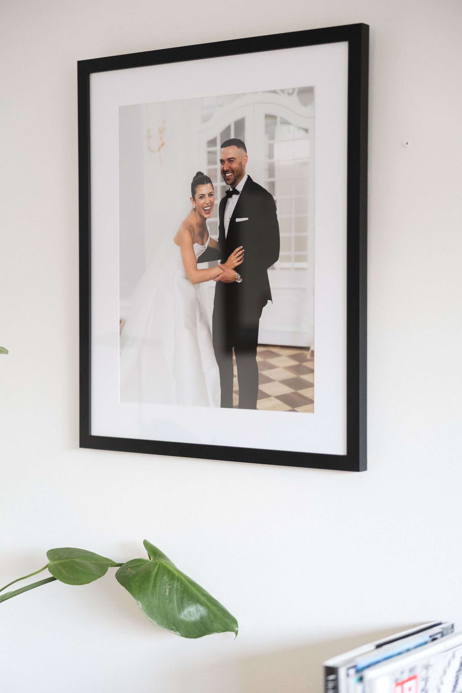 Elegant framed wedding portrait of smiling bride and groom in black frame on white wall.