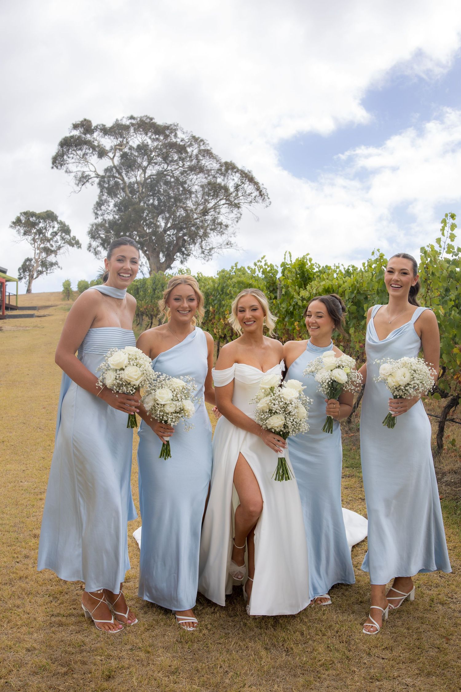 Bride in white gown with four bridesmaids in light blue dresses at a vineyard wedding.