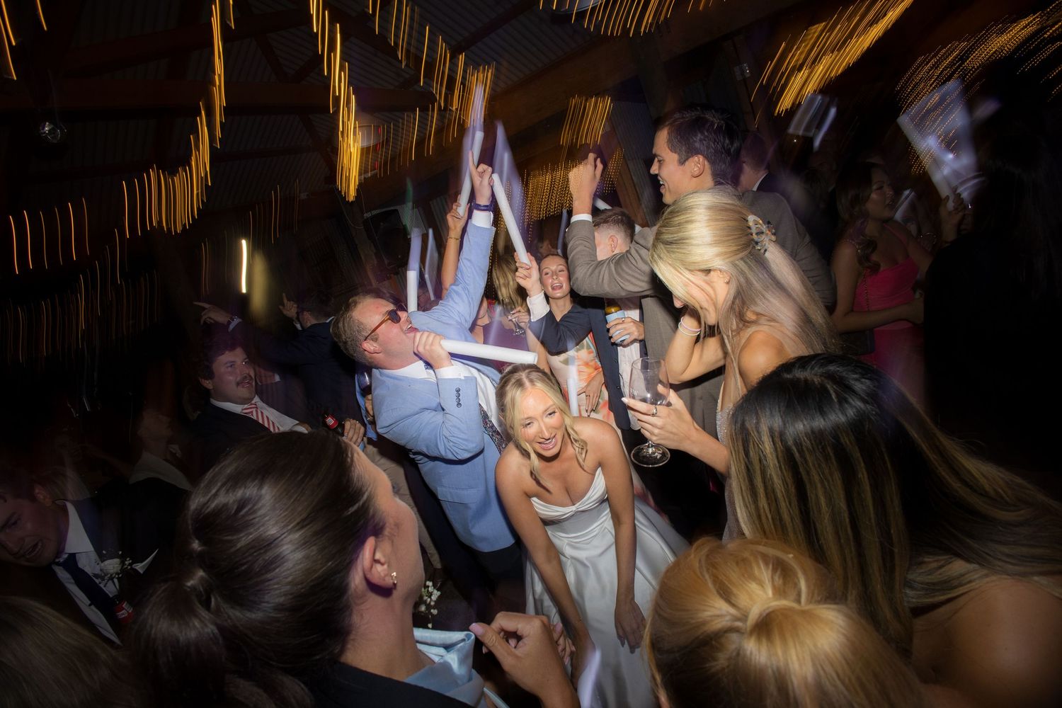 Energetic wedding reception dance floor packed with celebrating guests in warm venue lighting.
