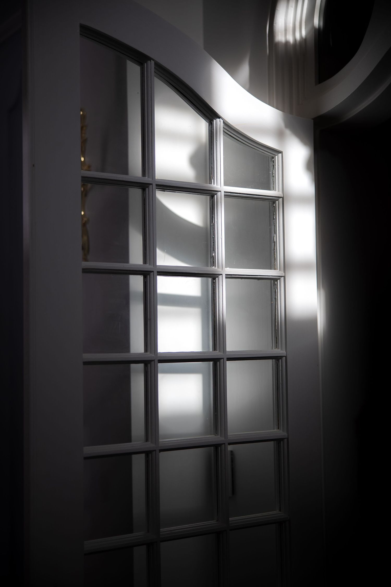Dramatic light and shadow falling across elegant white arched French door panels in wedding venue.