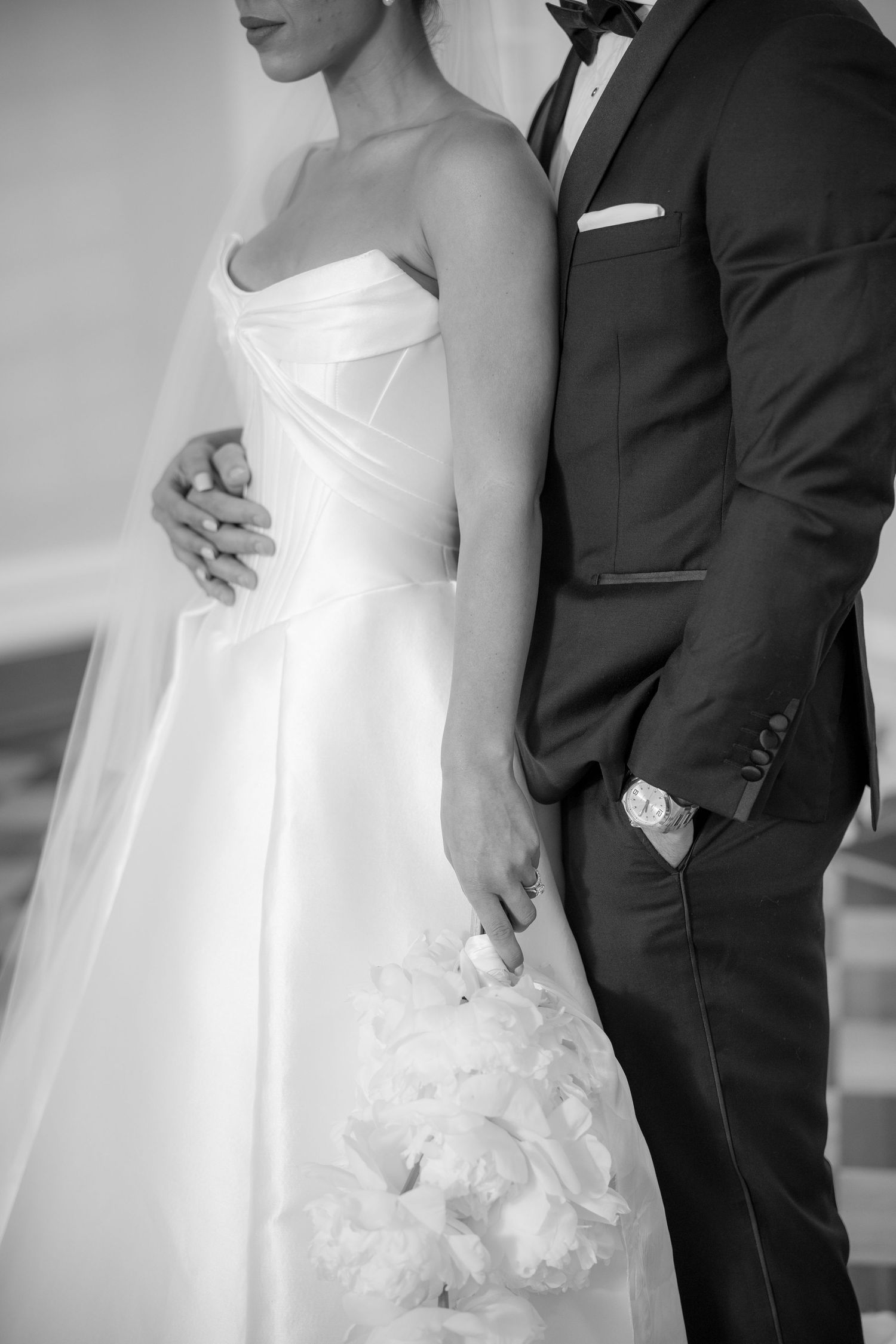 Black and white photo of bride and groom standing close, she holding white bouquet in elegant strapless gown.