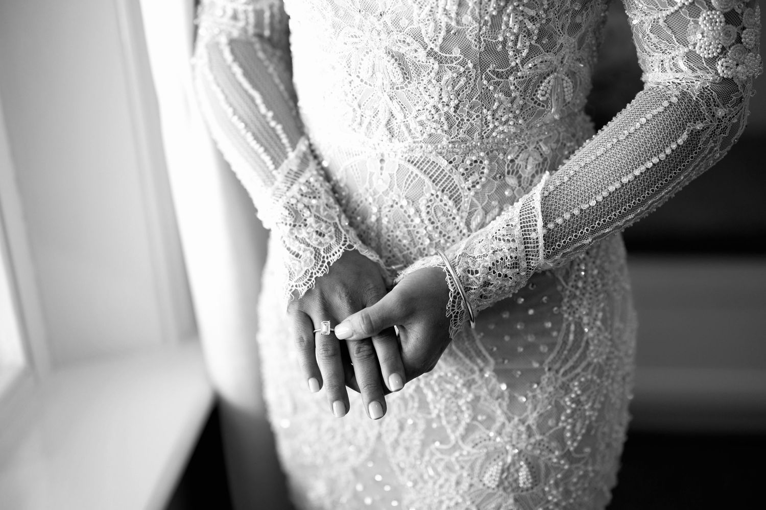 Close-up of a bride in a stunning beaded lace long-sleeve wedding gown, clasping her hands.
