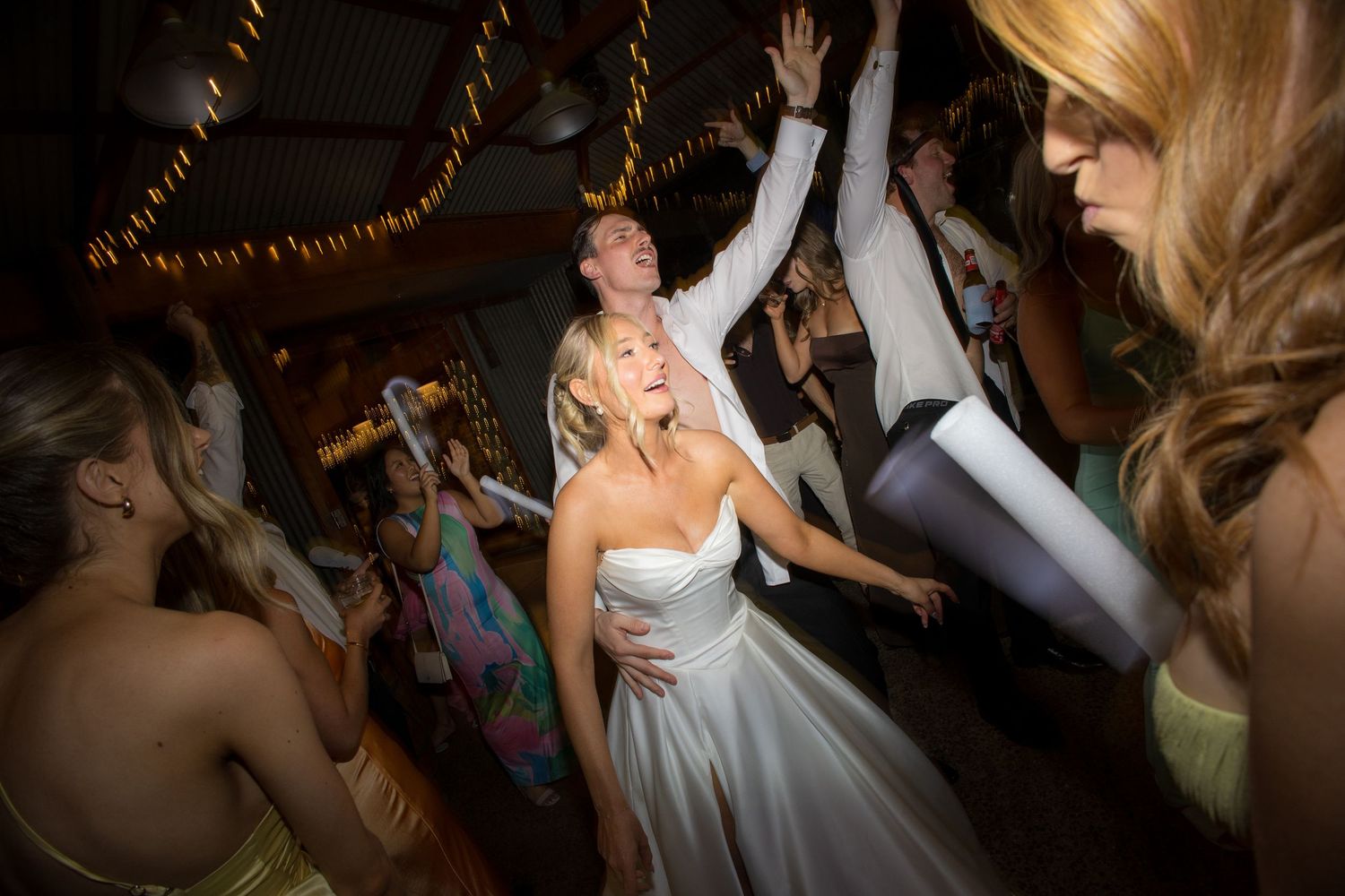 Bride in white strapless gown dancing energetically with guests at wedding reception.