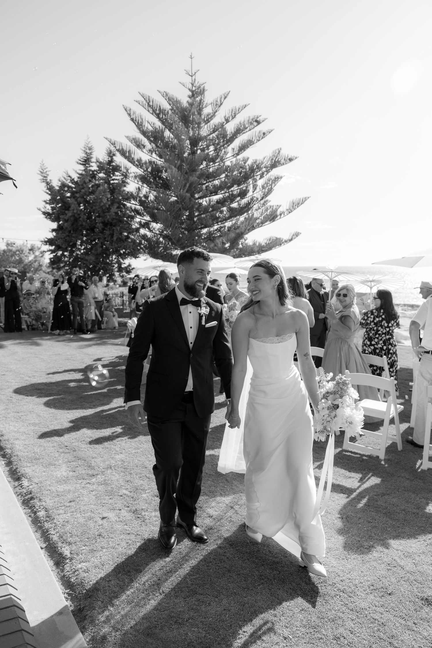 Bride and groom joyfully walking back down the aisle after their outdoor beach wedding ceremony in black and white.