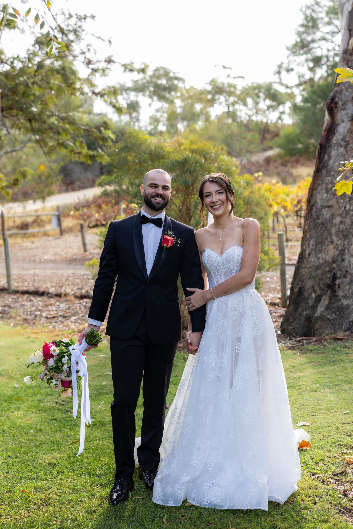 Smiling bride and groom holding hands in vineyard garden on their wedding day.