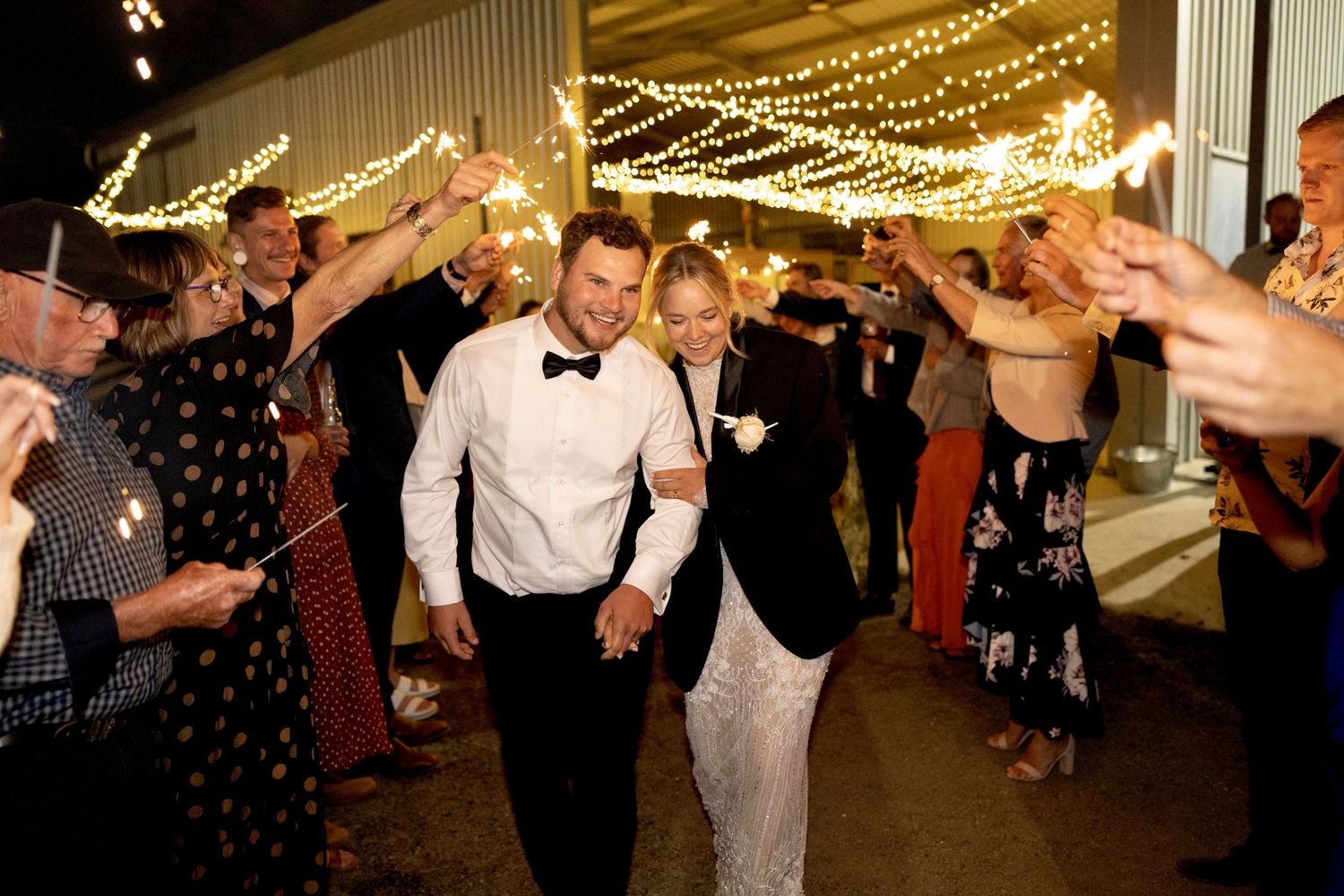 Newlyweds walk through a sparkler tunnel surrounded by cheering guests at wedding reception.